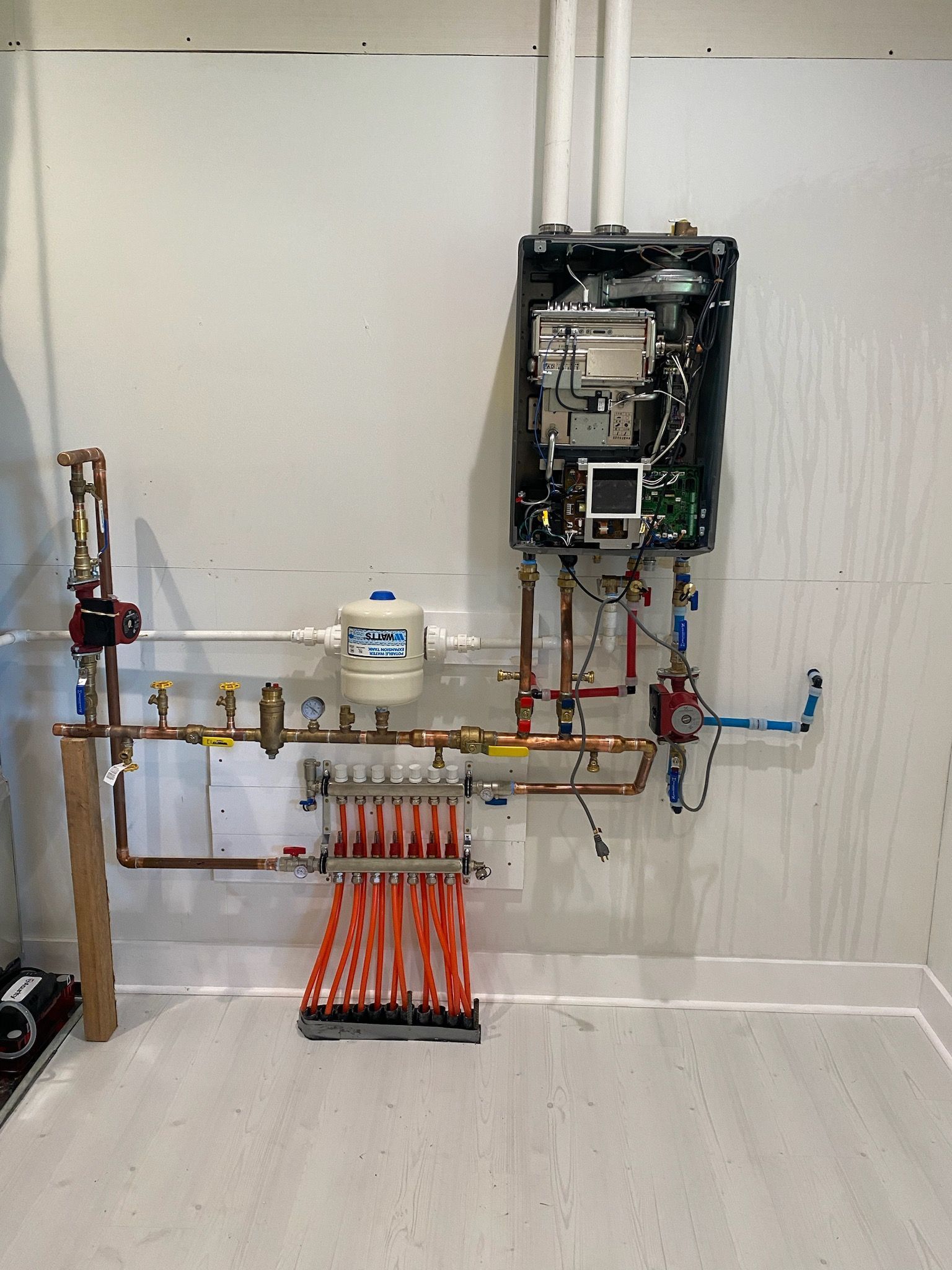 Water heater and related plumbing installed on a white wall, including copper pipes, valves, and a distribution manifold.