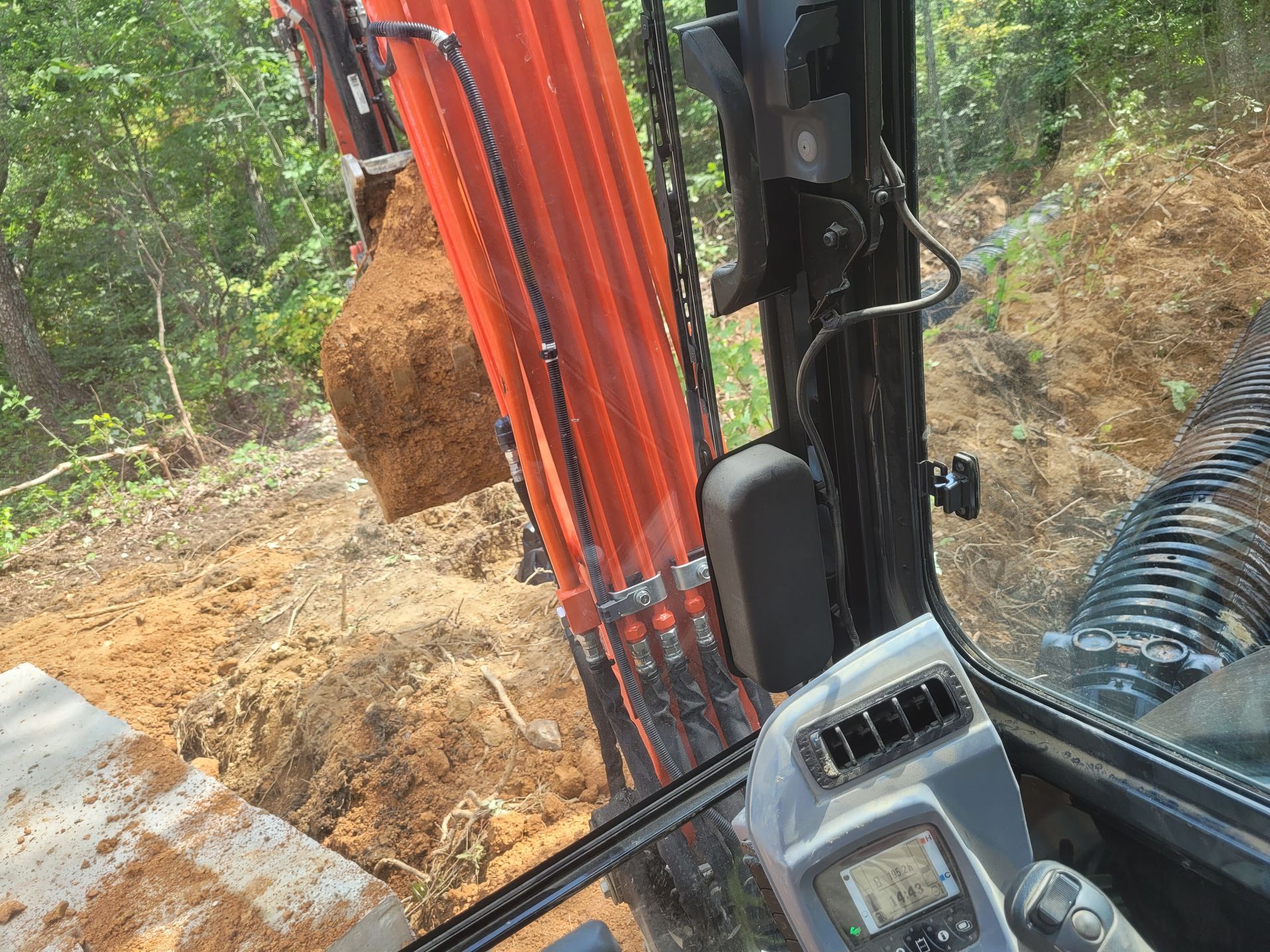 View from inside an excavator cab; digging dirt. Orange arm, black cab interior.