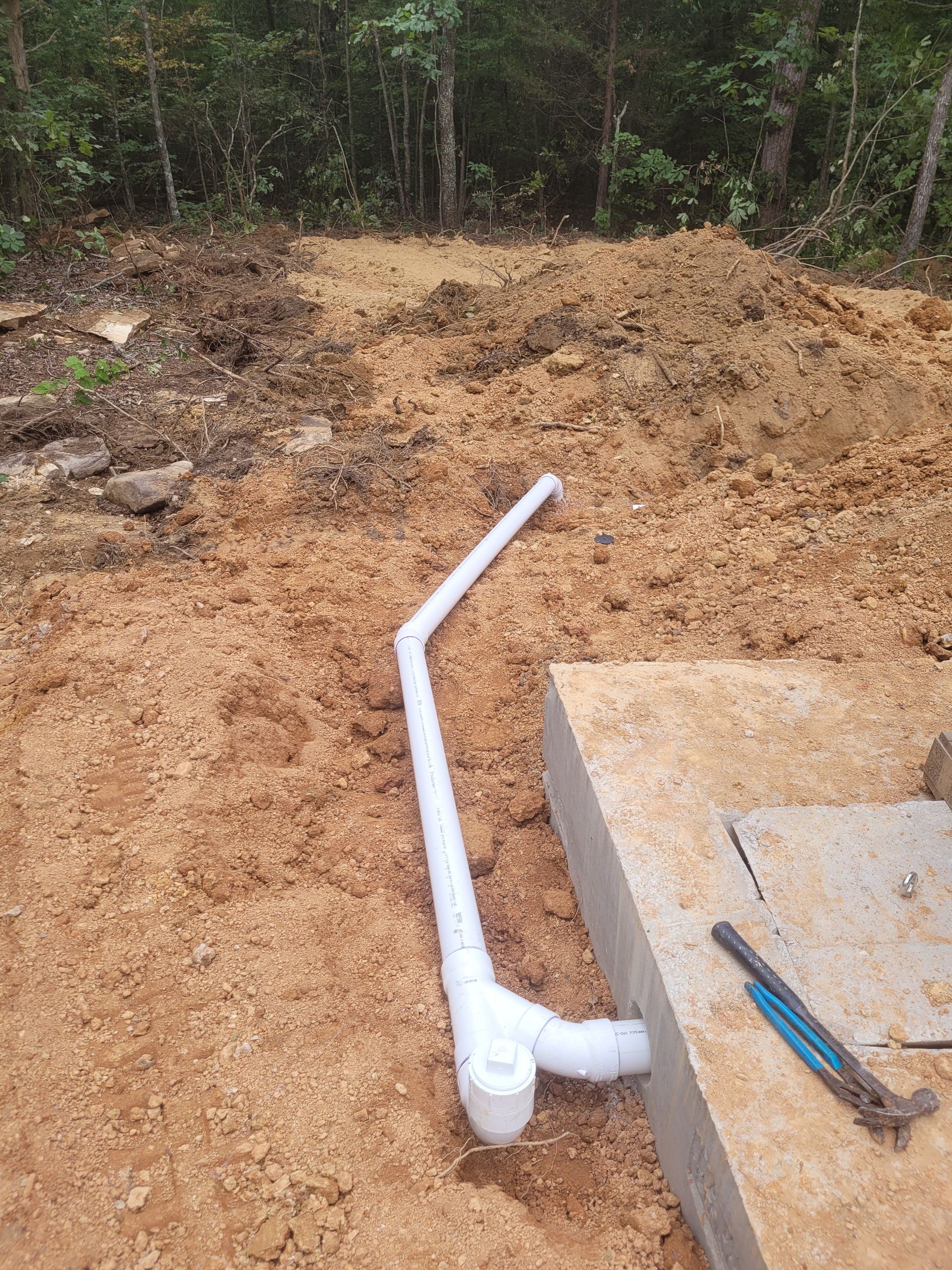 White PVC pipes extending from a concrete structure into dirt and mulch.