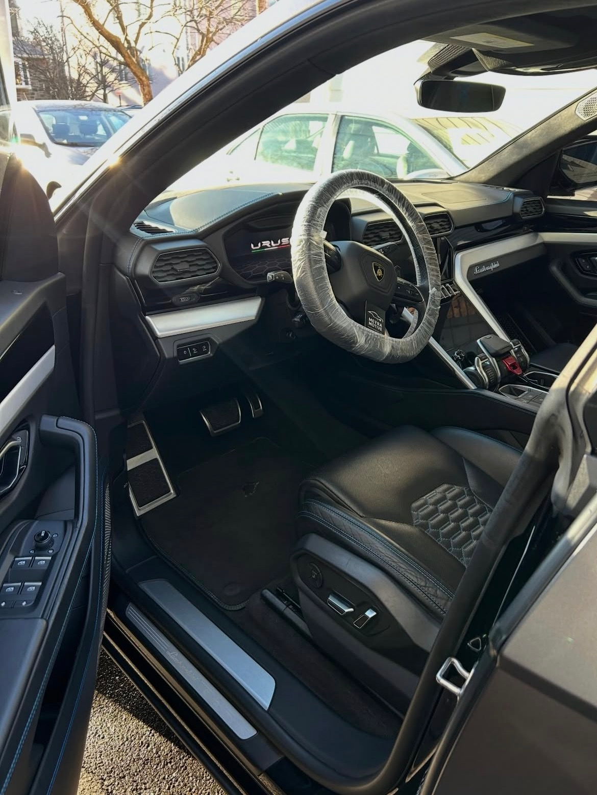 Car interior with open driver door, black seats, and a steering wheel wrapped in a protective cover.