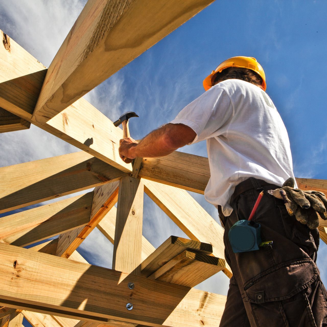 A man wearing a hard hat is working on a wooden structure