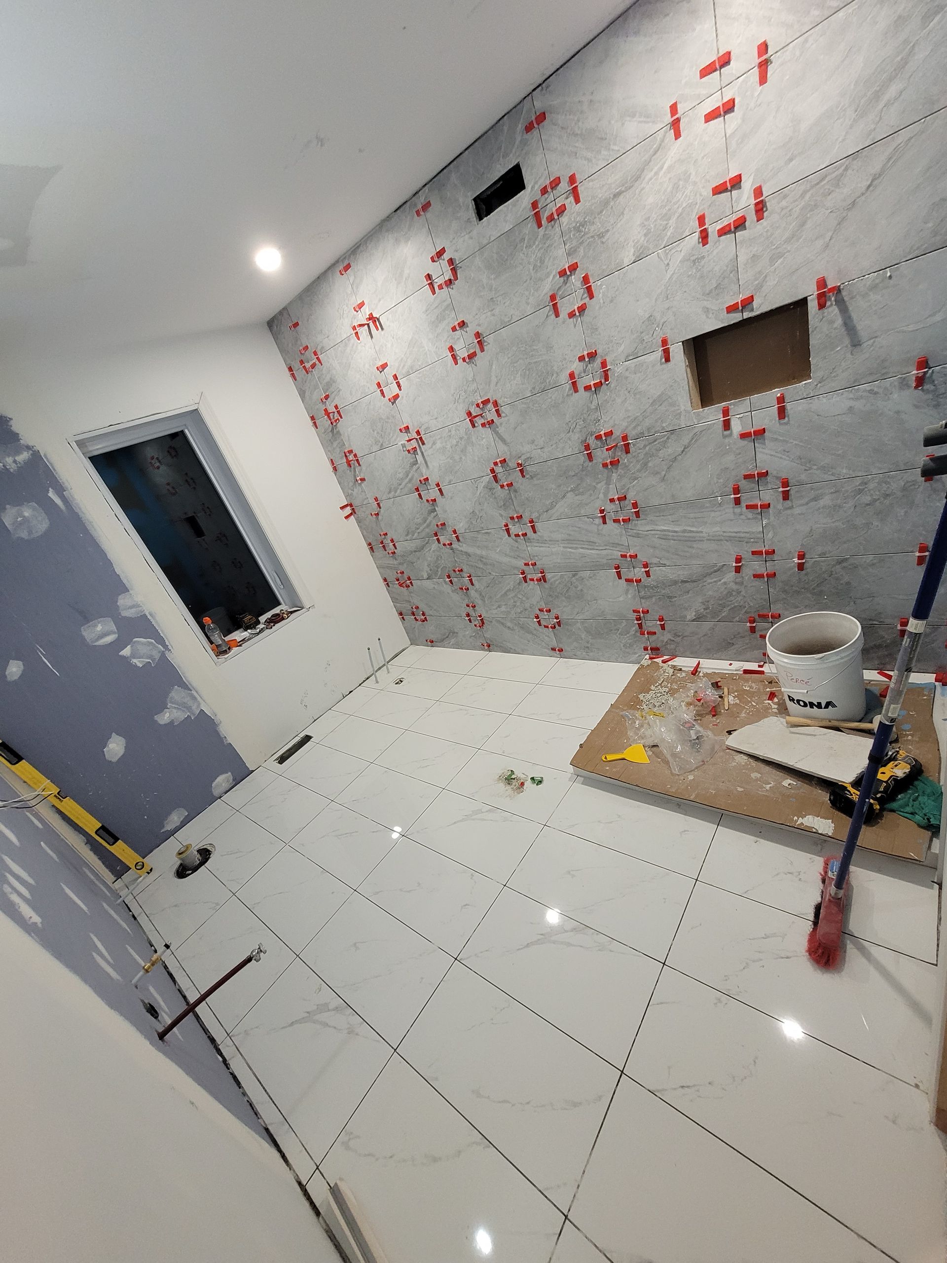 Une salle de bain en construction avec du carrelage blanc au sol et aux murs.