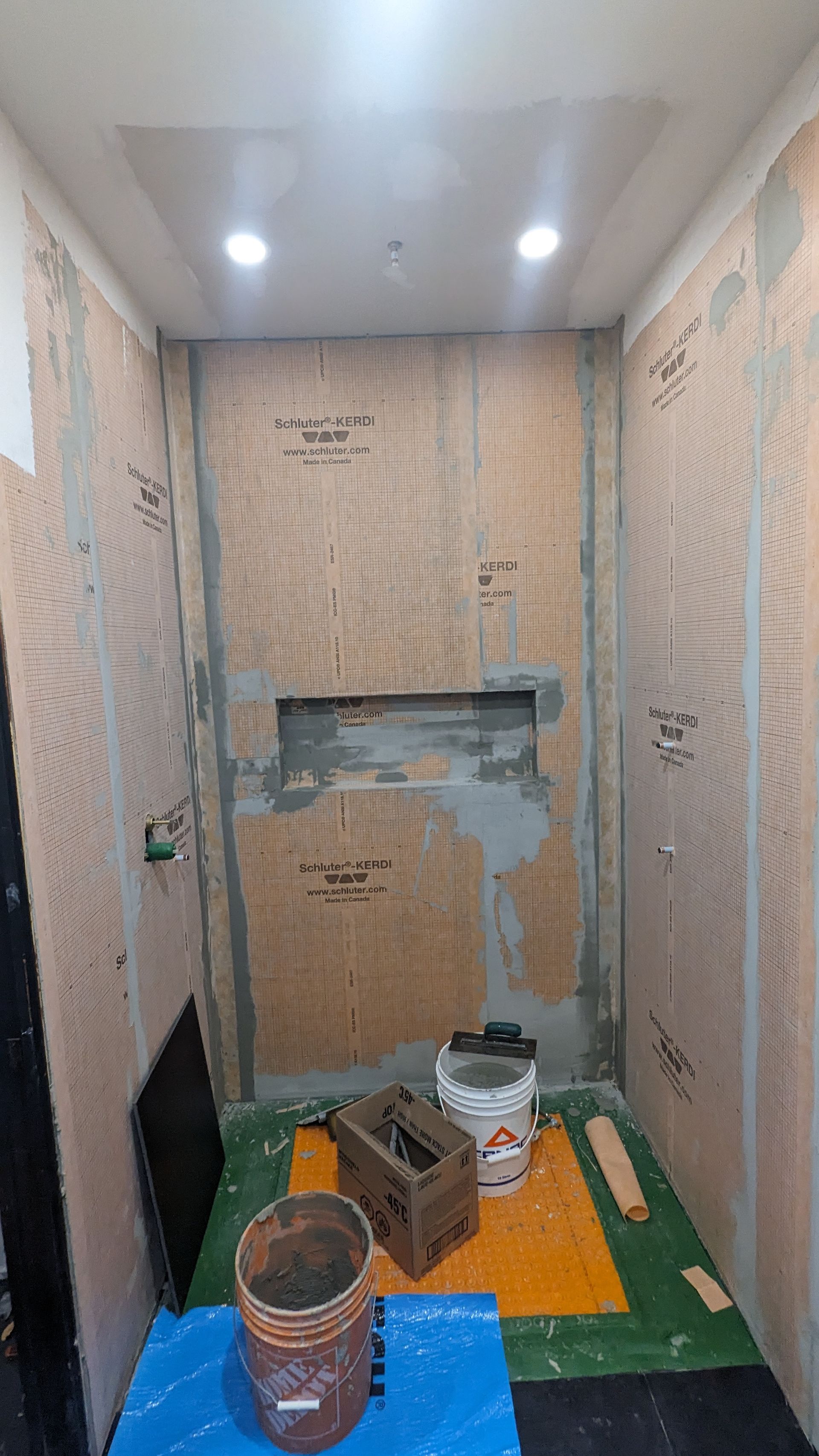 Une salle de bain en construction avec un seau de ciment sur le sol.