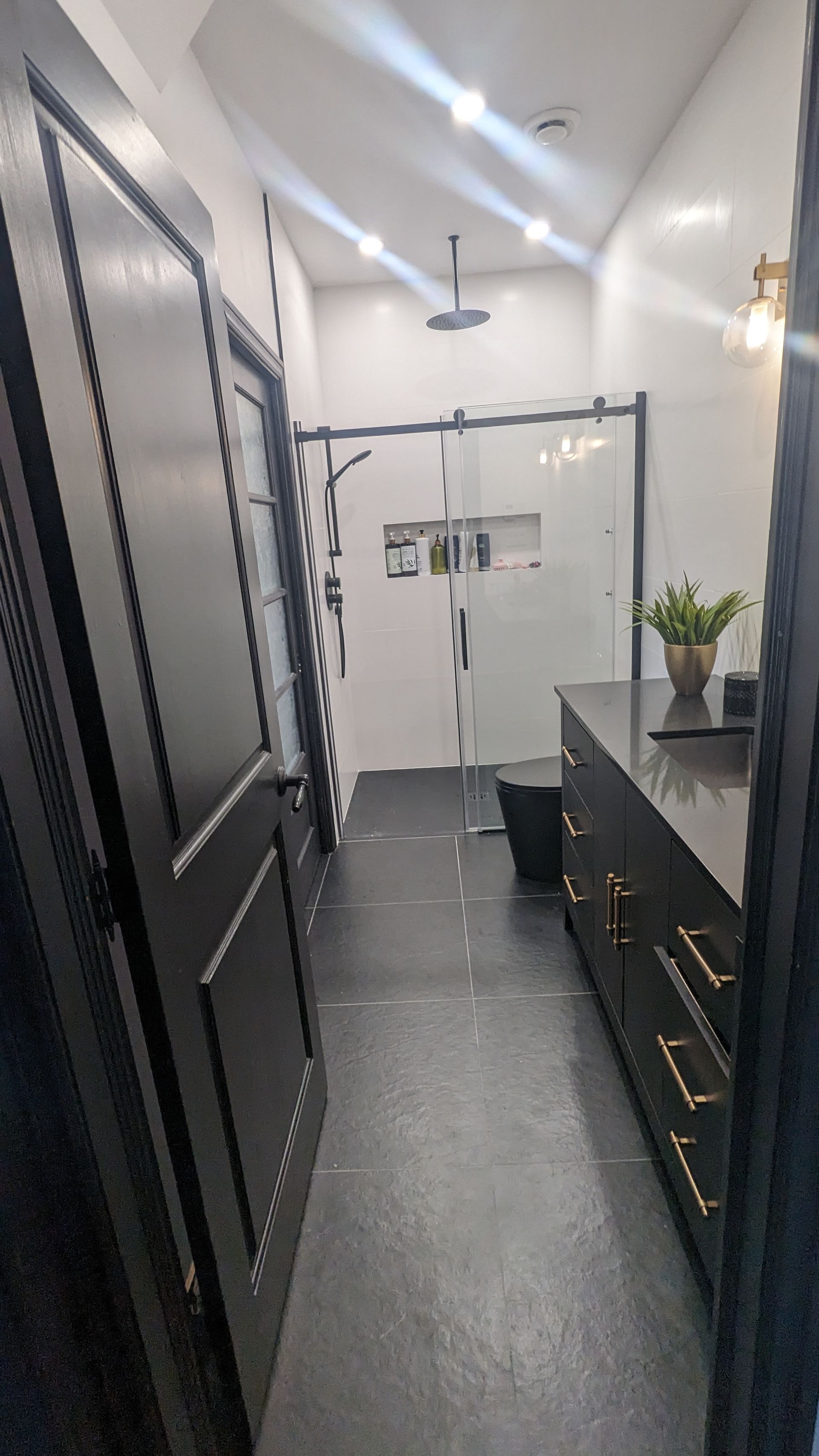 Un long couloir menant à une salle de bain avec des armoires noires et des portes noires.