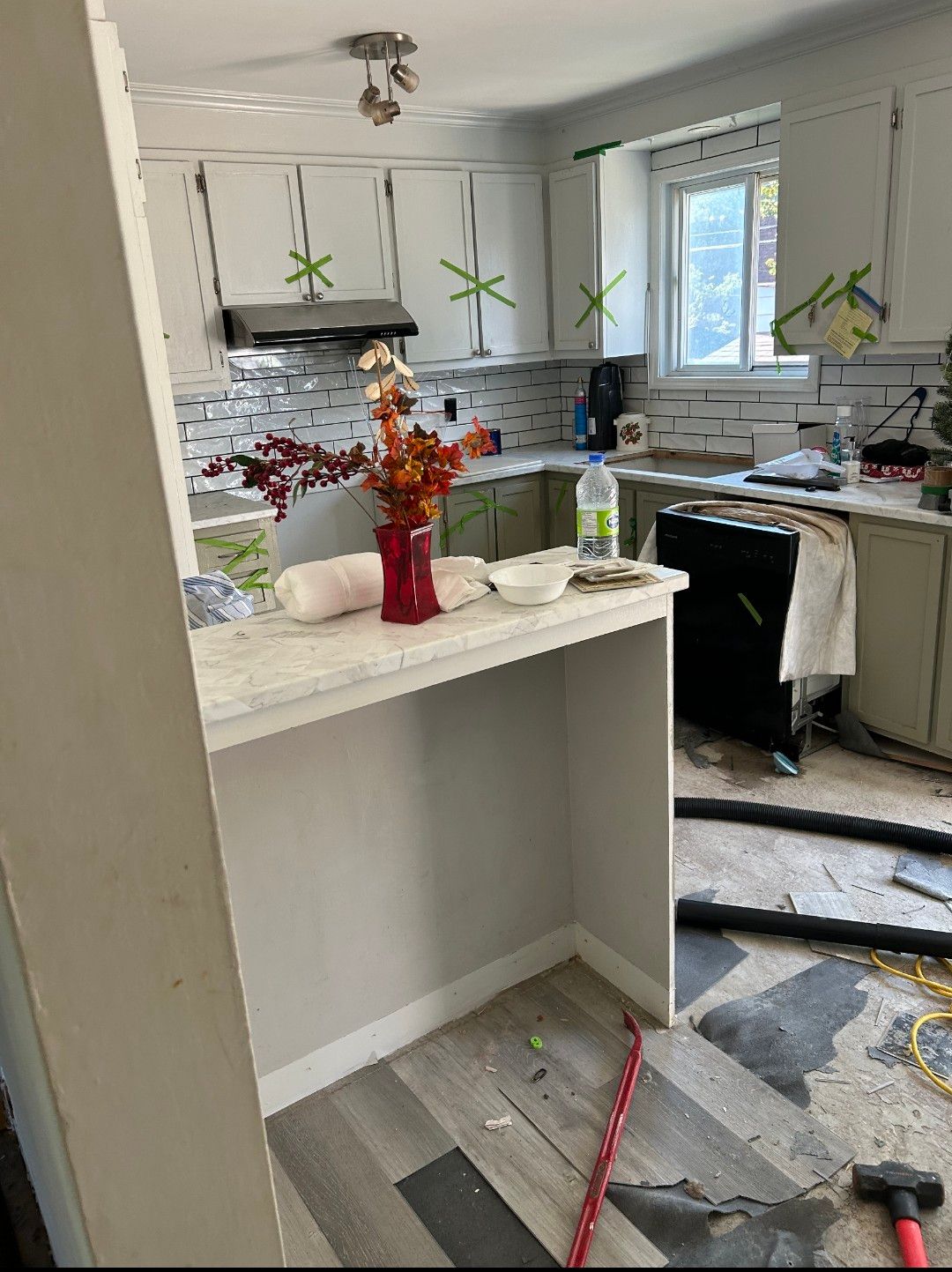 Une cuisine avec un marteau sur le sol et un vase de fleurs sur le comptoir.