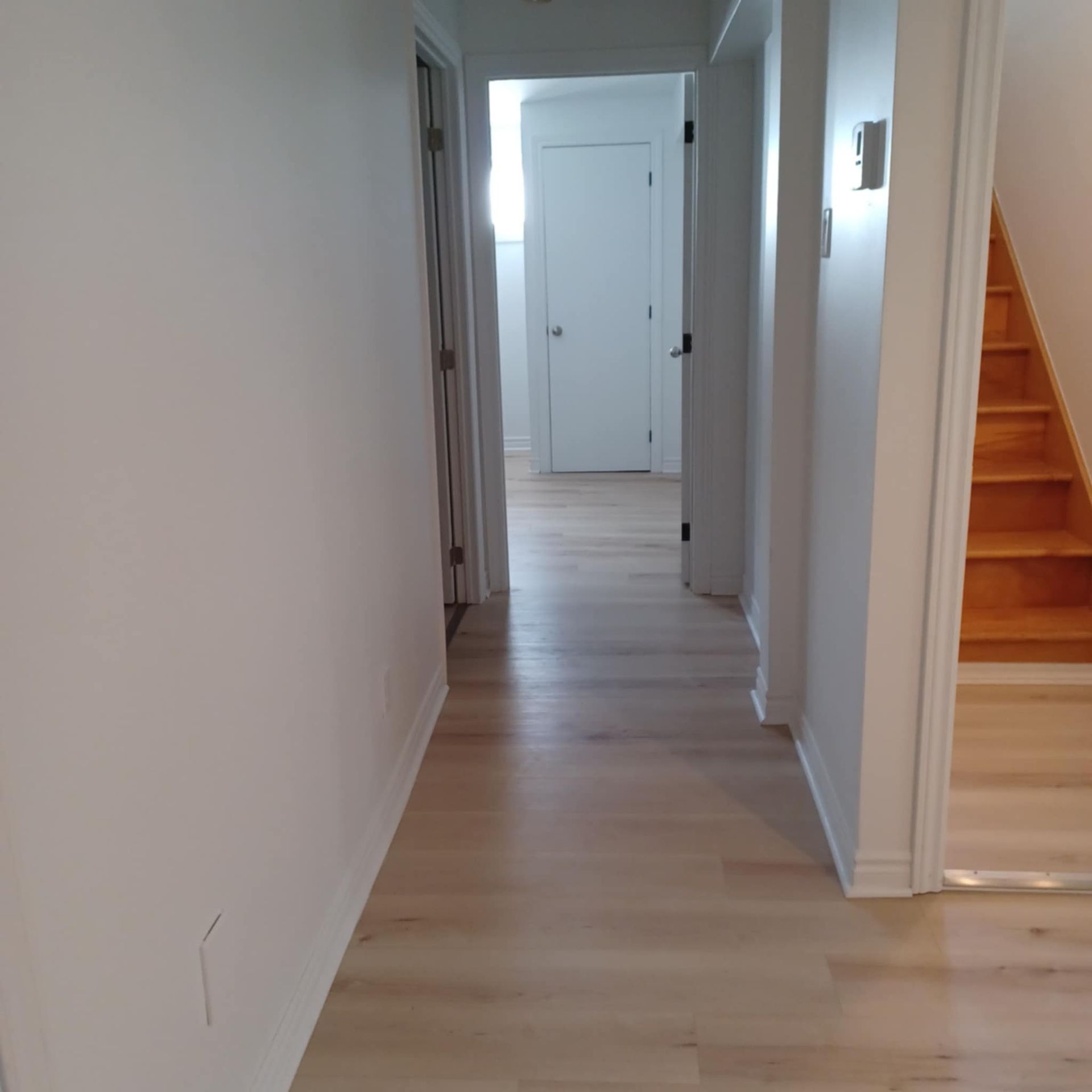 Un couloir avec du parquet et des murs blancs