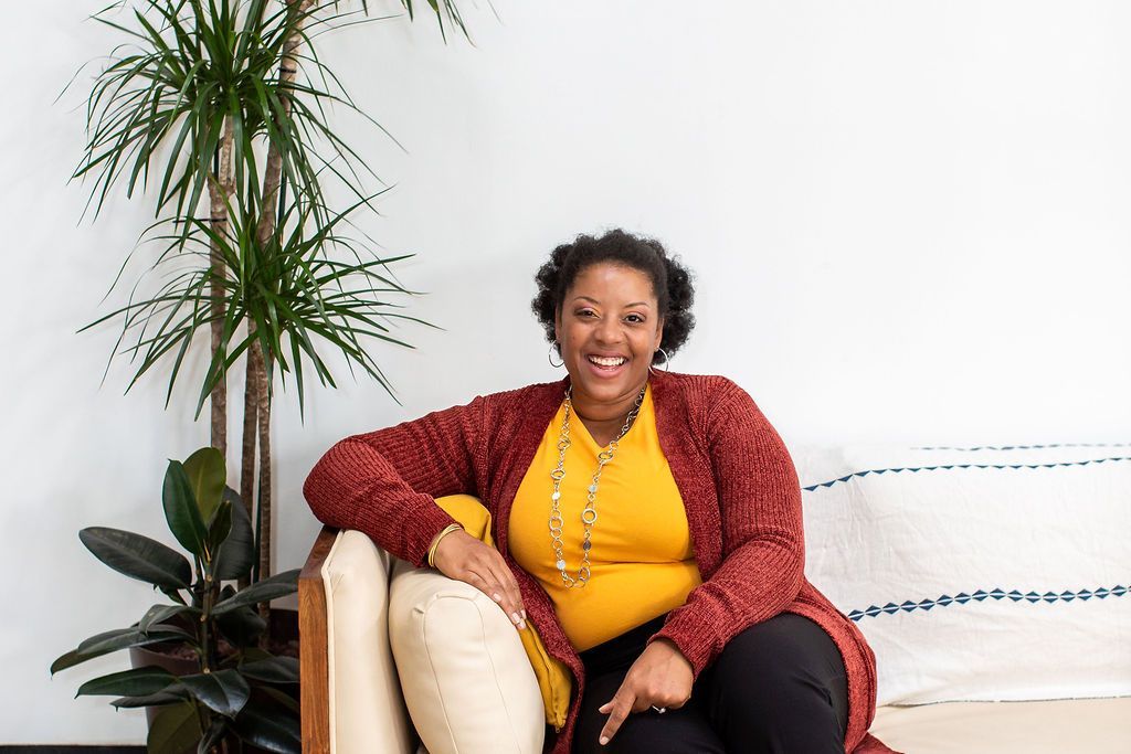 A woman is sitting on a couch next to a plant.