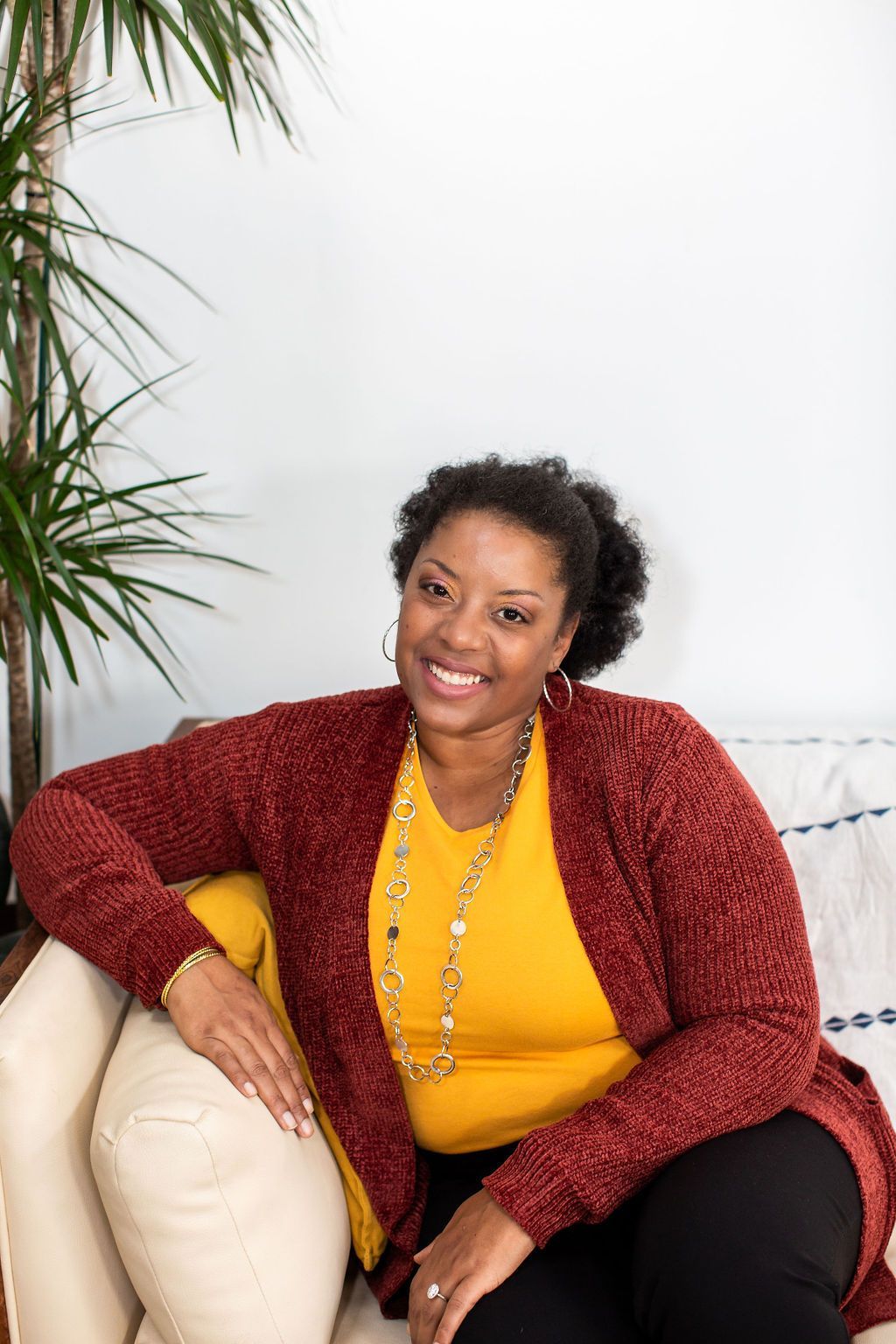 A woman is sitting on a couch wearing a red cardigan and a yellow shirt.