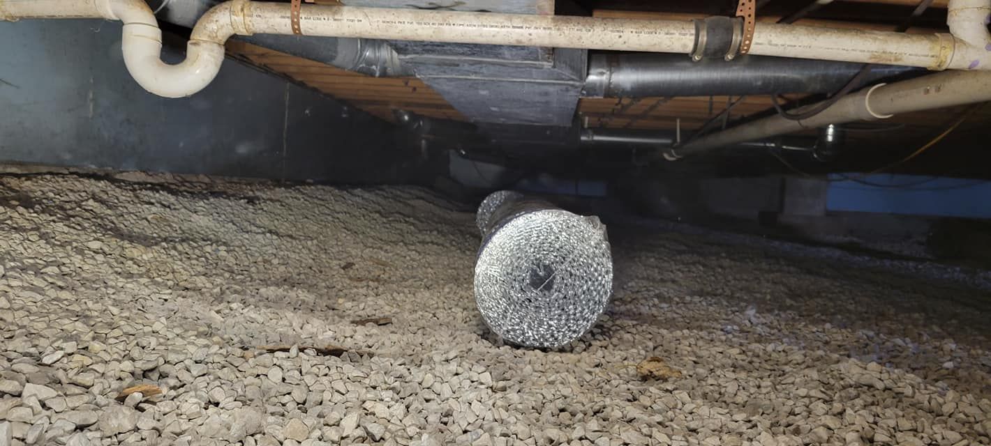 A pipe is laying on the ground under a house.