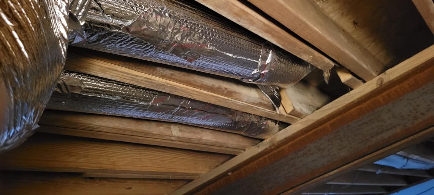 A close up of a wooden ceiling with aluminum foil ducts.
