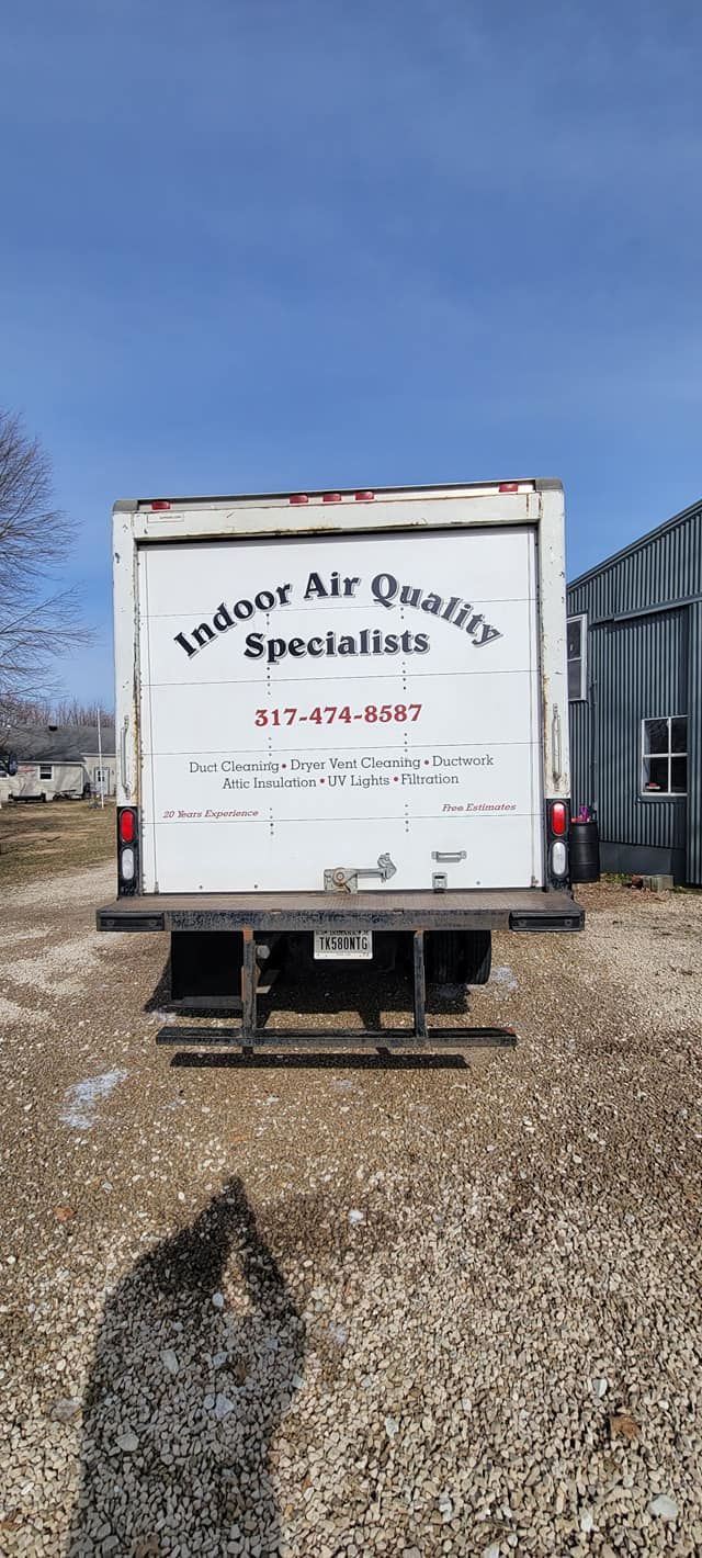 A white truck is parked in a gravel lot in front of a building.