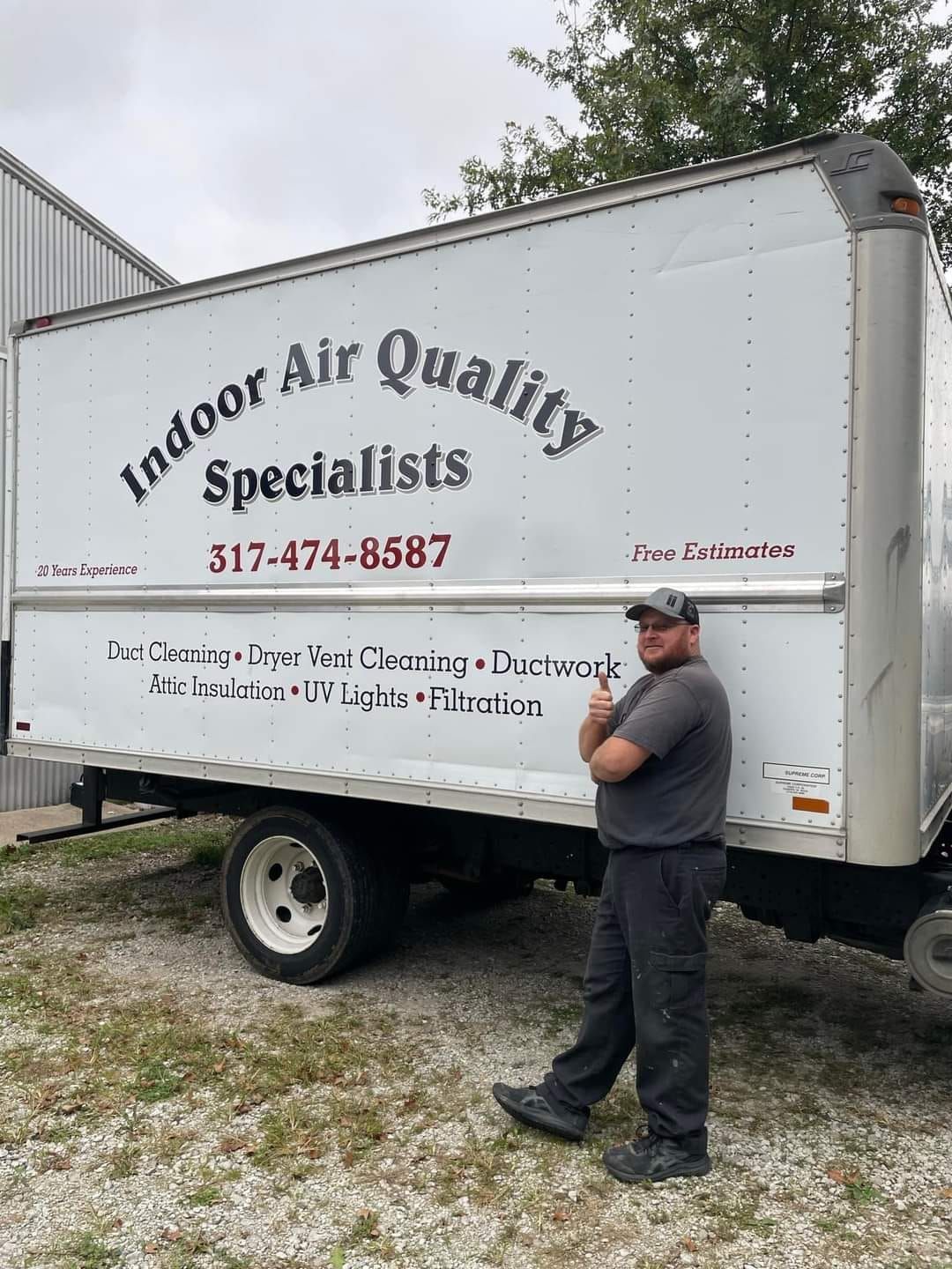 A man is standing in front of a white truck that says indoor air quality specialists.