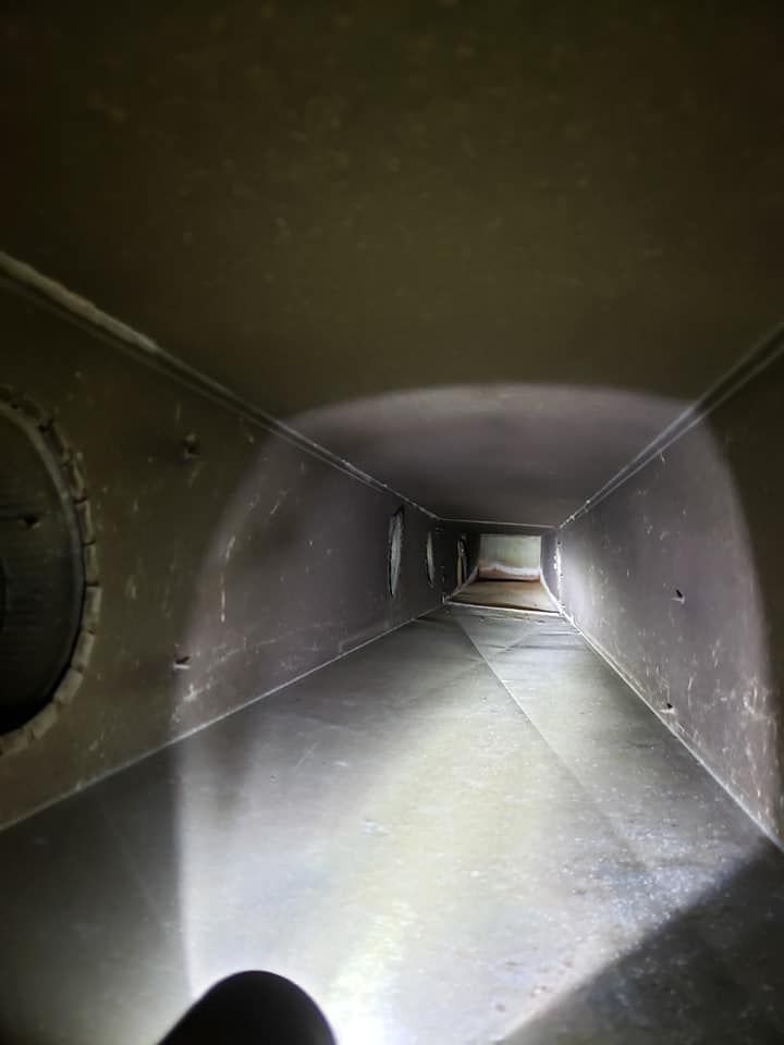 A person is holding a flashlight in a duct that looks like a tunnel.