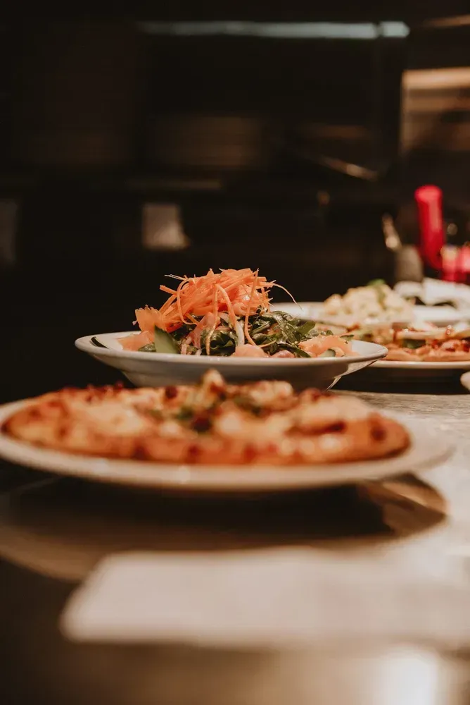 A Pizza and a Salad Are on Plates on a Table — Zachary's in Noosaville, QLD