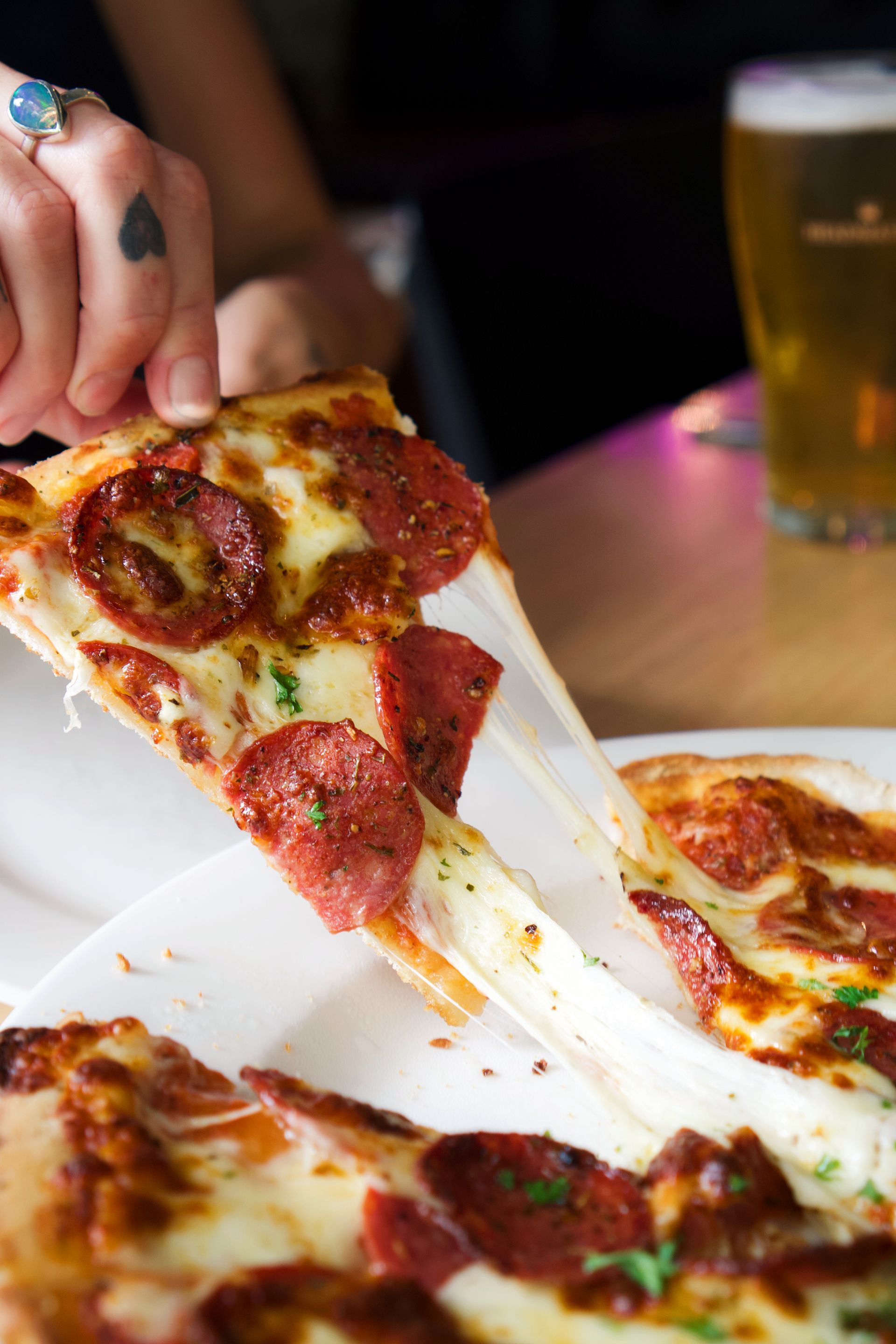 A Pizza With a Slice Taken Out of It on a Wooden Table — Zachary's in Noosaville, QLD