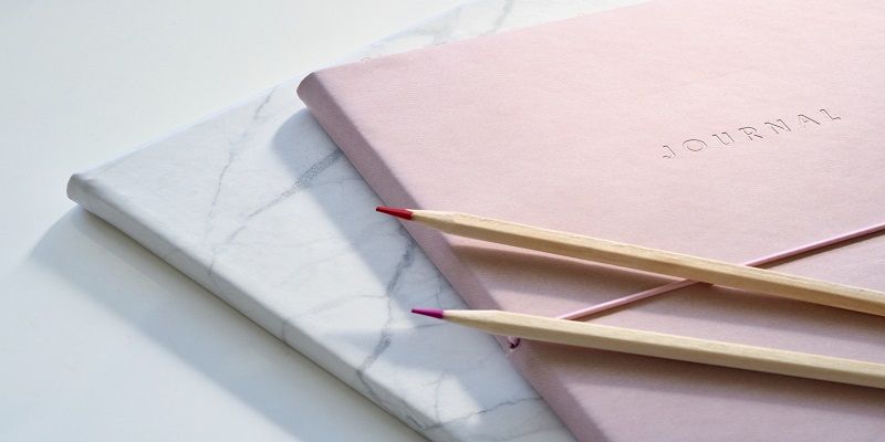 two notebooks and two pencils are stacked on top of each other on a table .