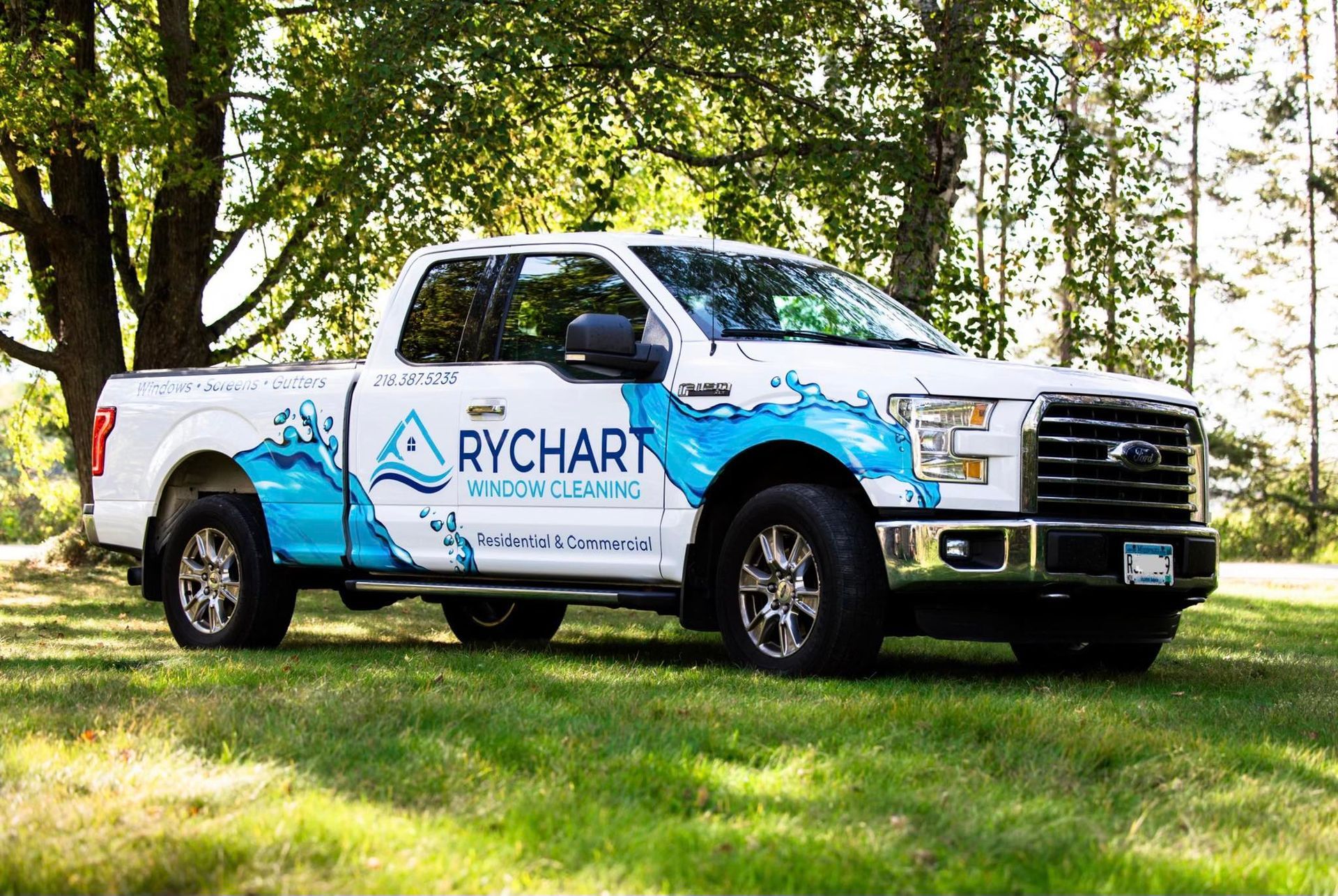White pickup truck with blue water graphic, RYCHART pool cleaning logo on side, parked on grass.