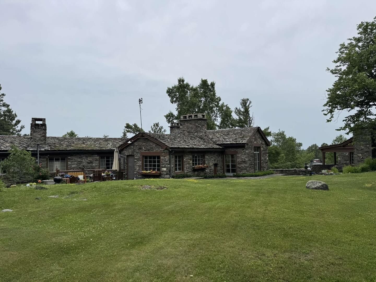 Stone house with multiple chimneys, on a grassy lawn, under a cloudy sky.