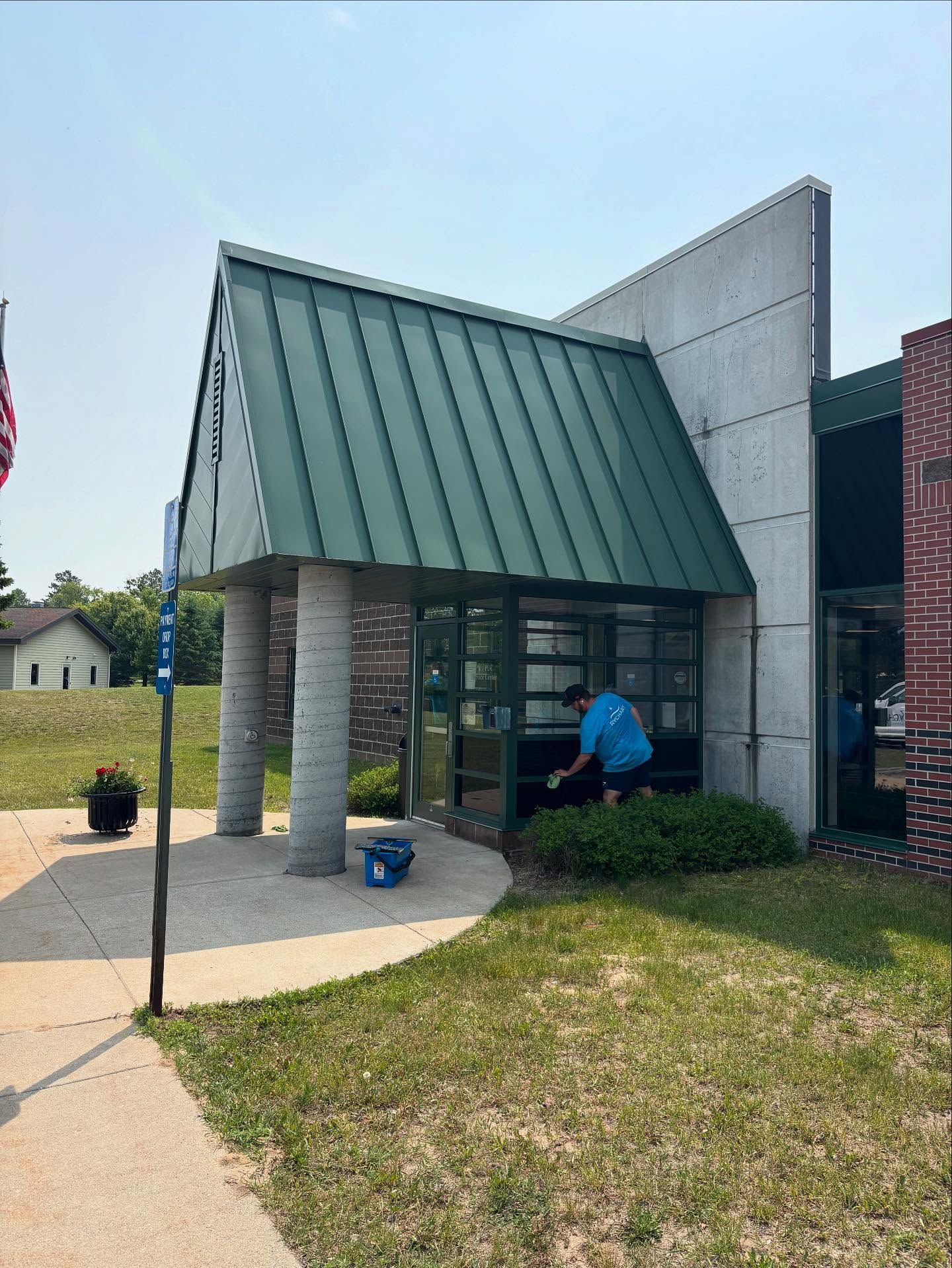 Person cleaning glass door of a building with green roof; sunny day.