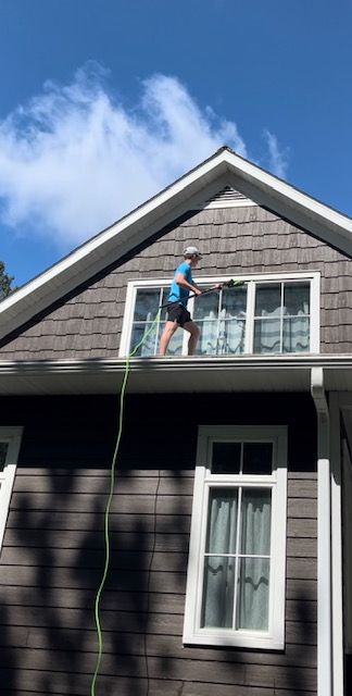 Man washing windows on a house roof with a green hose on a sunny day.