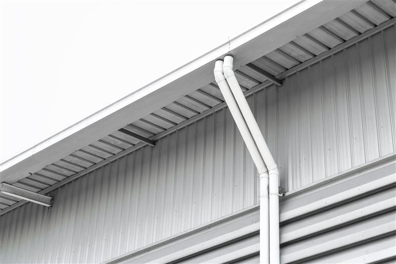 White building exterior with vertical siding and white drain pipes.