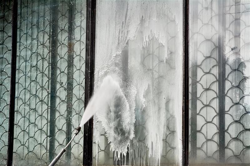 A person spraying water onto a window with decorative panels using a pressure washer.