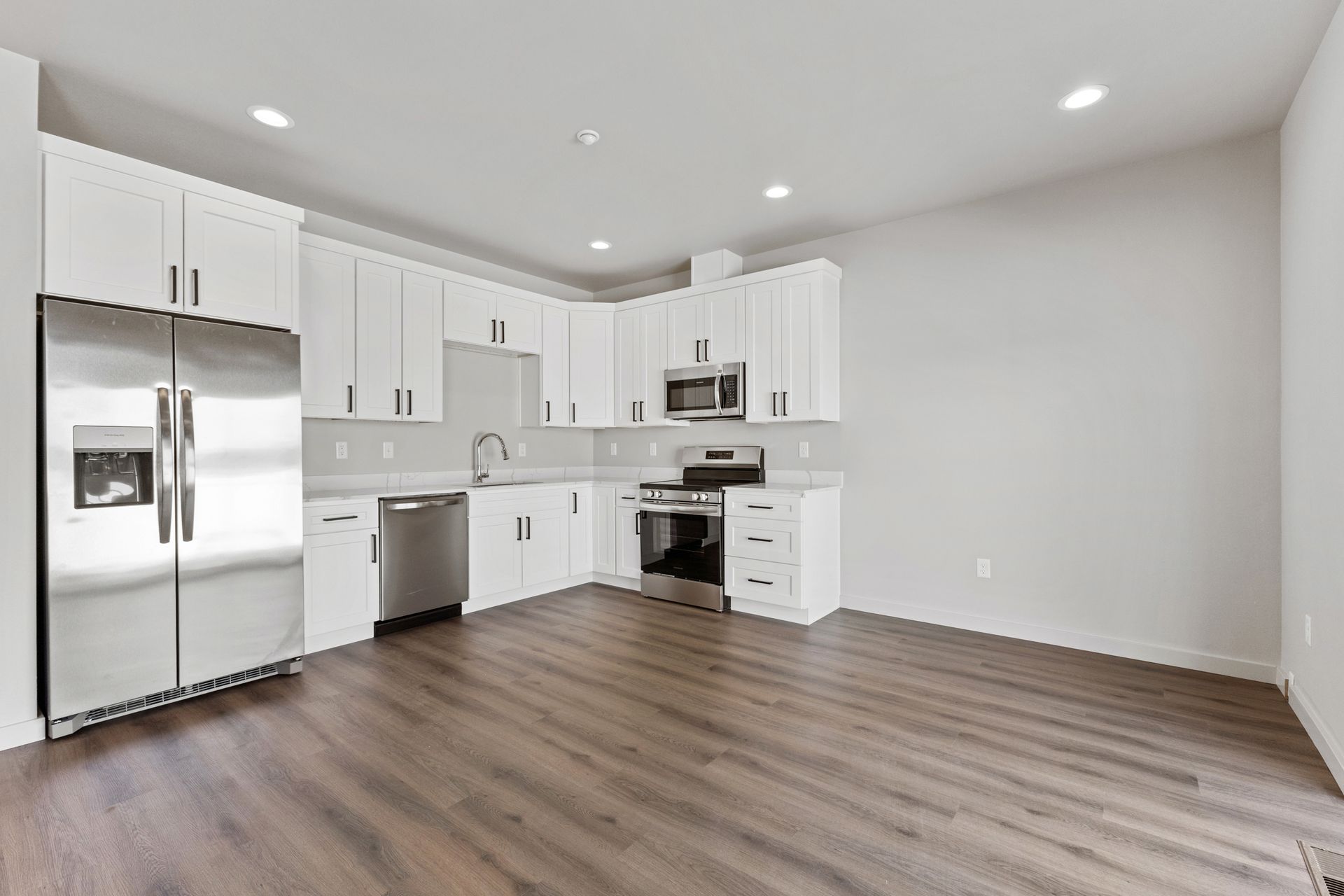Modern kitchen with white cabinets, stainless steel appliances, and wood flooring.