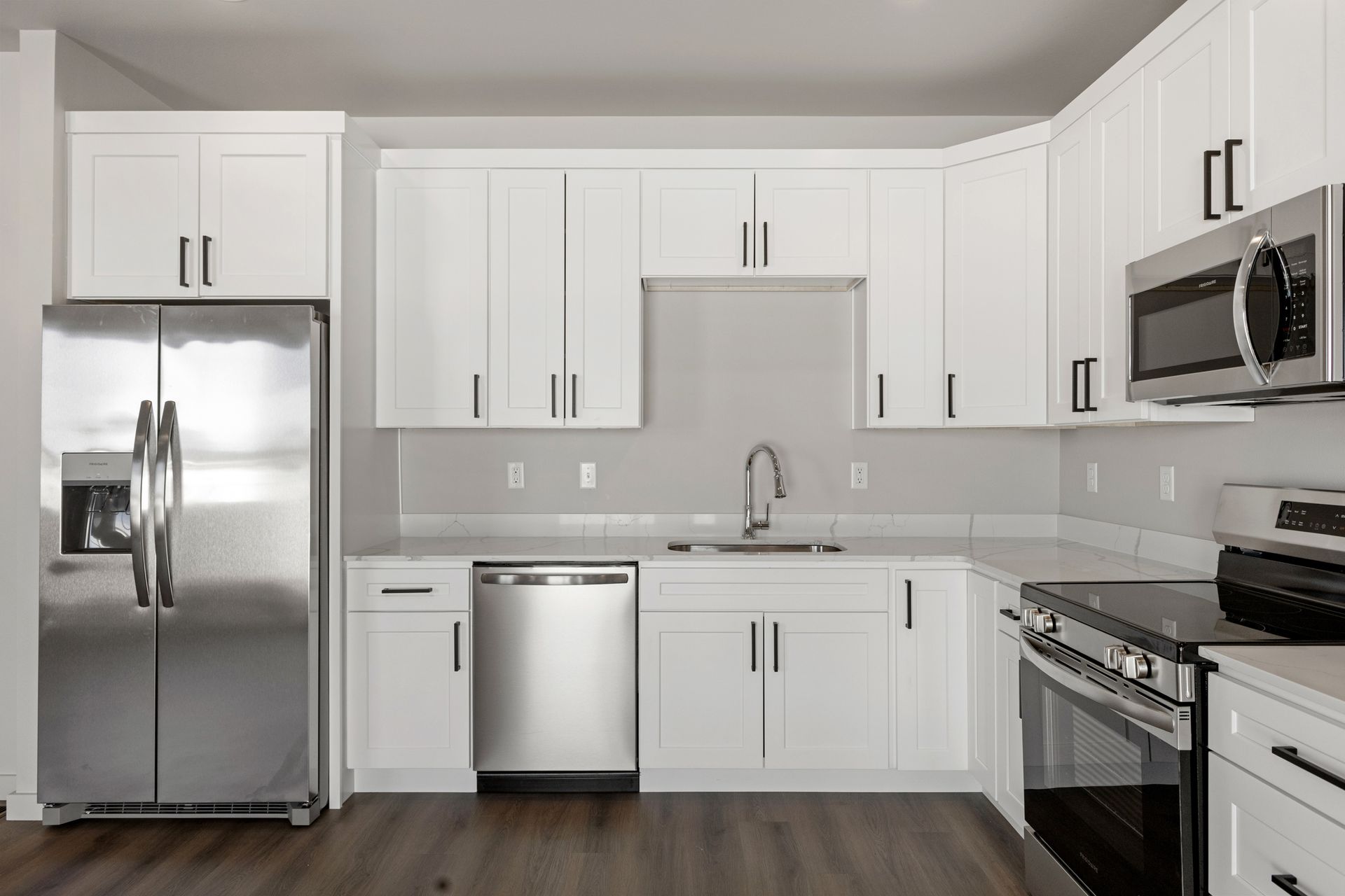White kitchen with stainless steel appliances and dark hardware.