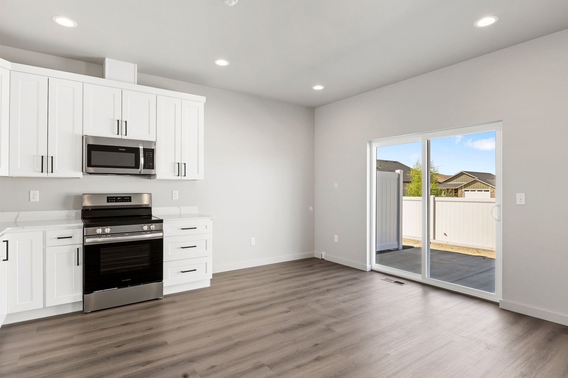 Bright kitchen with white cabinets, stainless steel appliances, sliding glass door to a backyard.