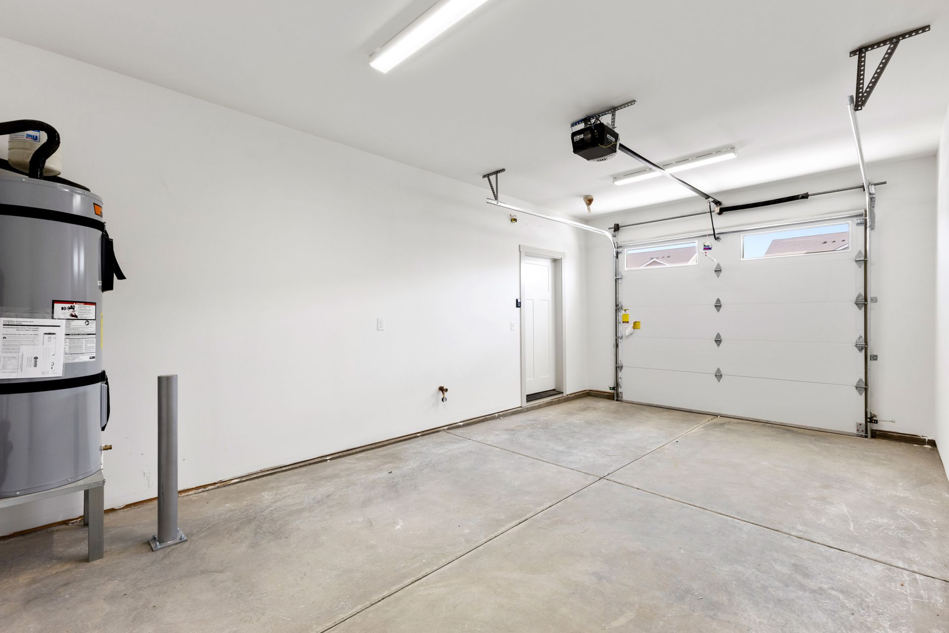Empty, bright garage with a water heater, garage door, and a door to the outside.
