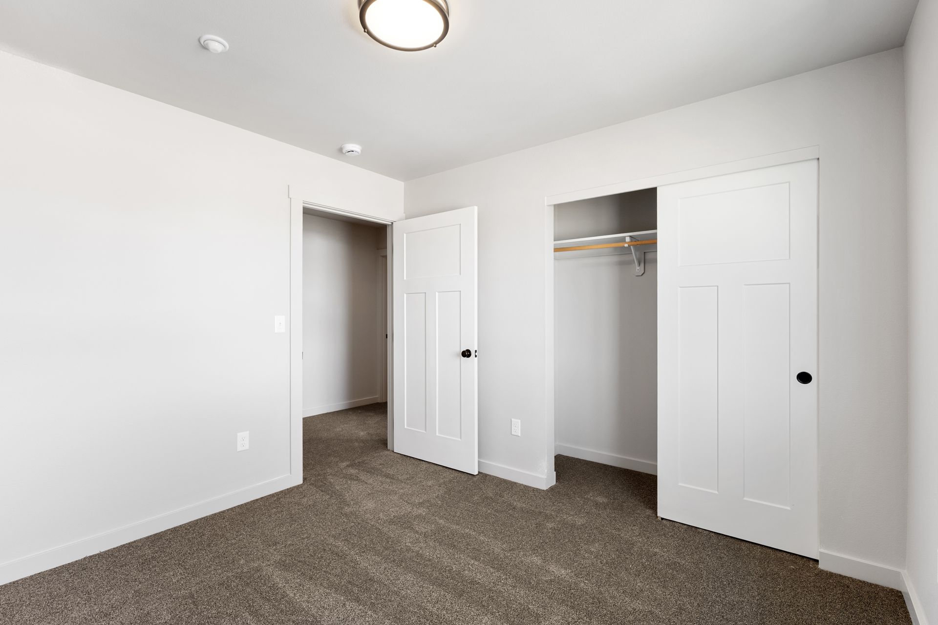 Empty bedroom with light-colored walls, carpet, closet with sliding doors, and a closed door to another room.
