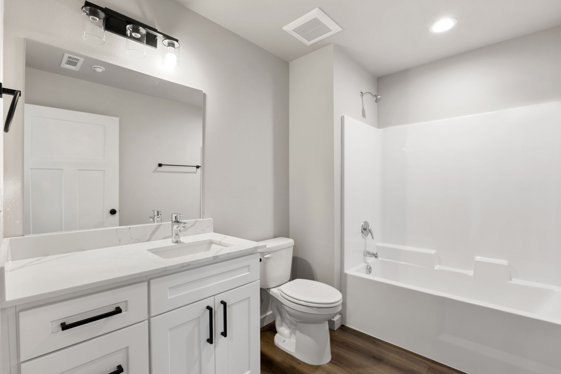 Bathroom with white vanity, toilet, and tub/shower; gray walls and brown floor.