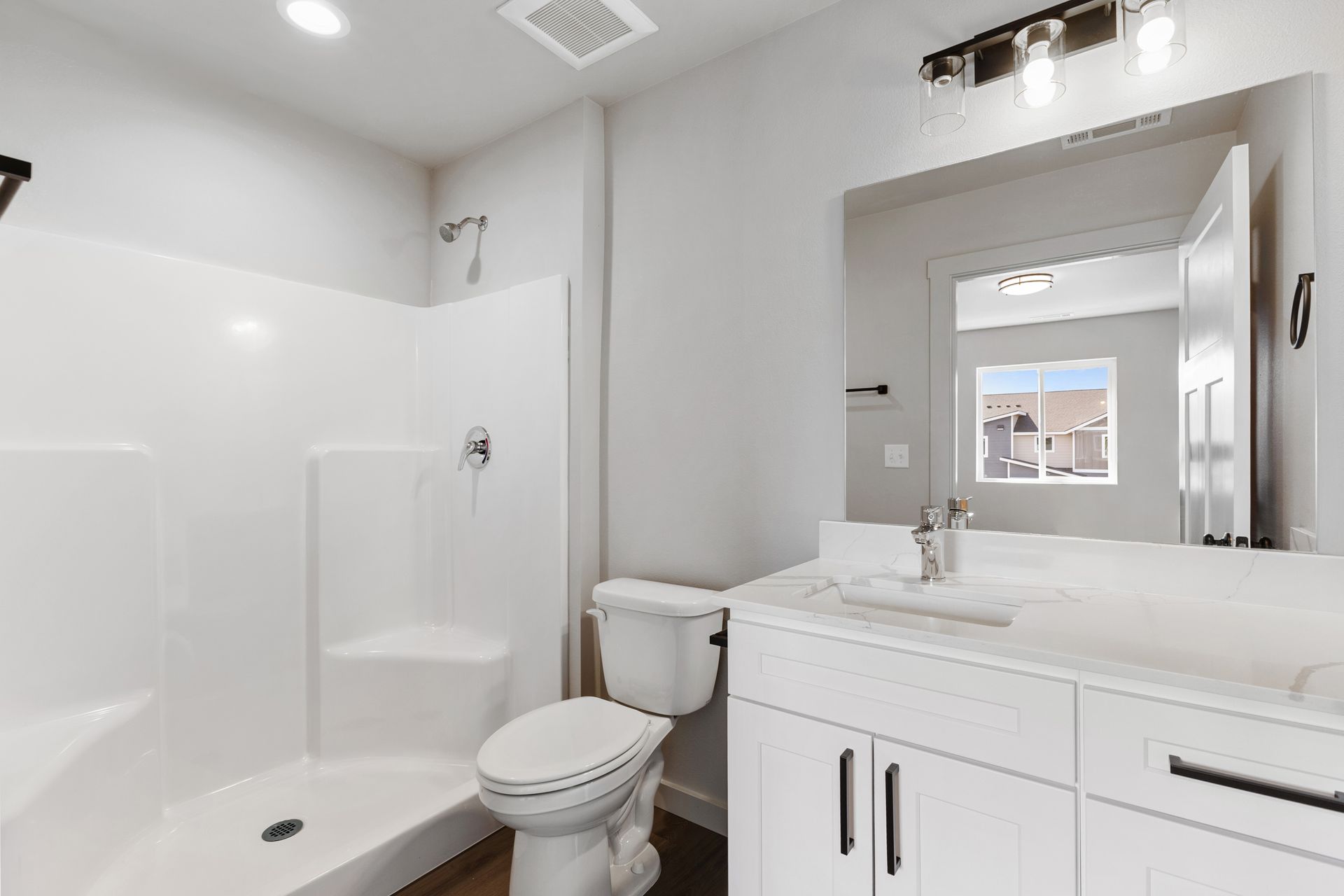 White bathroom with shower, toilet, and vanity with a large mirror.