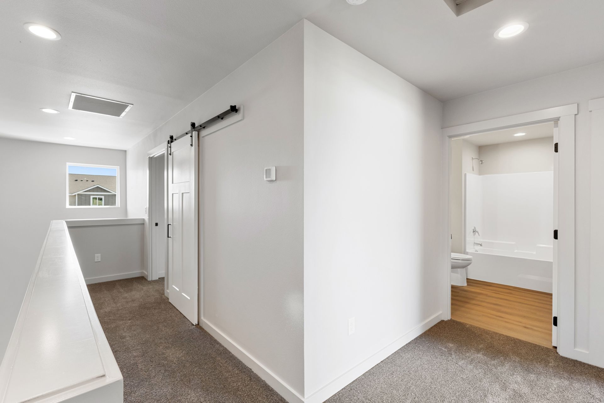 Hallway with carpet, white walls, sliding door, and a bathroom entrance.