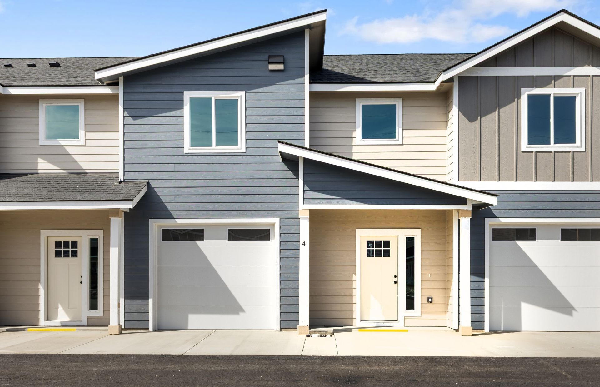 Row of townhouses with neutral siding, slanted roofs, and attached garages.