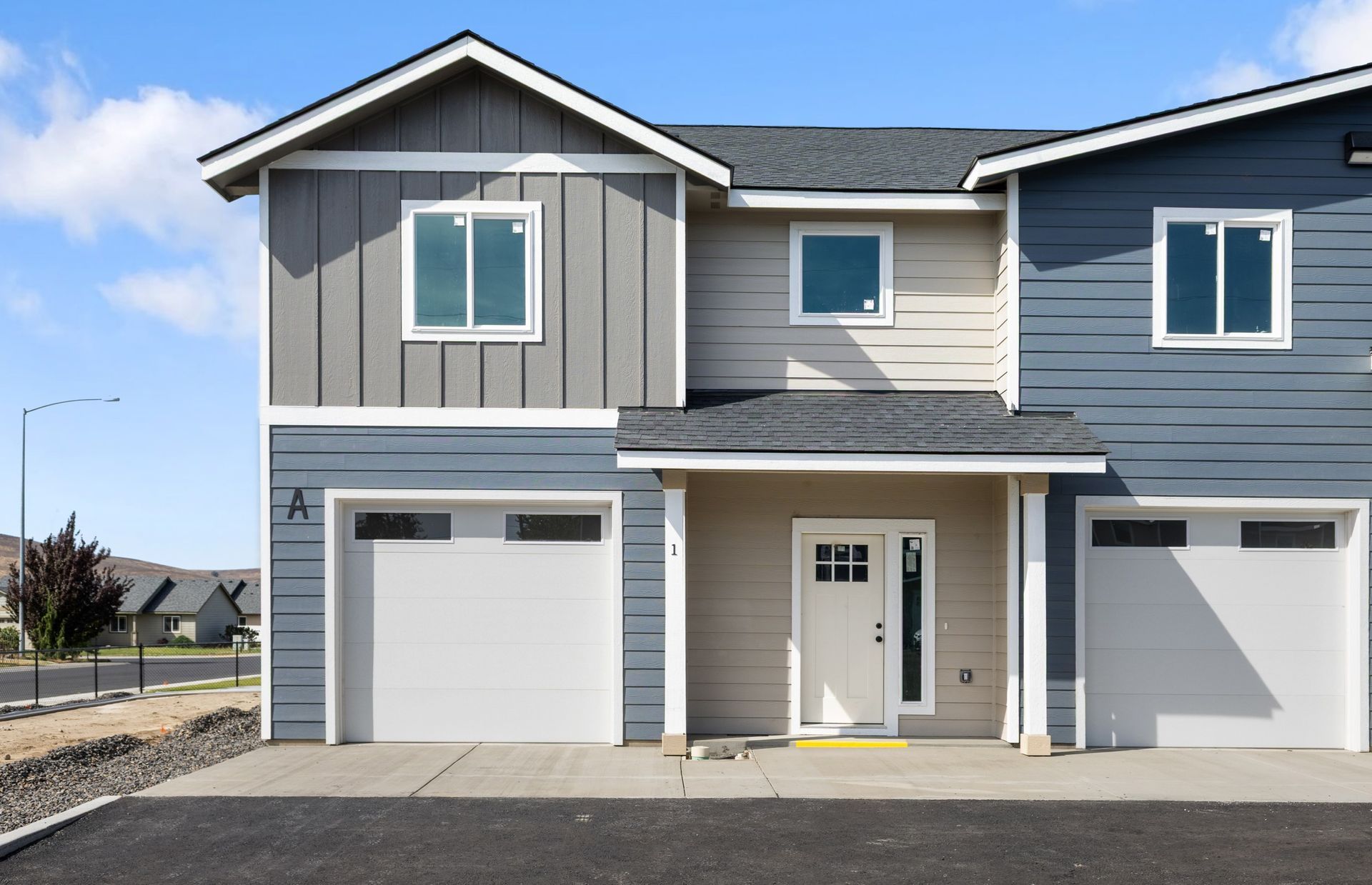 Townhouse exterior with blue and beige siding, white garage doors, and front door.