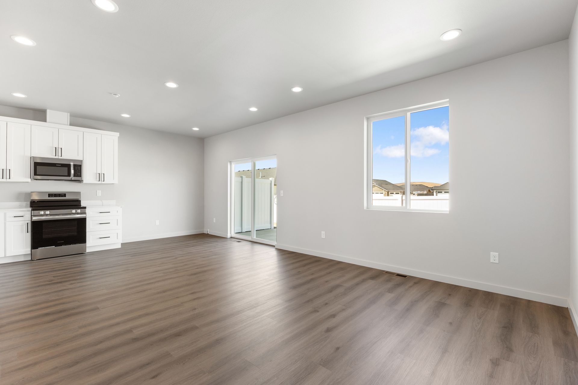 Modern kitchen and living area with white cabinets, stainless steel appliances, and wood-look floors.