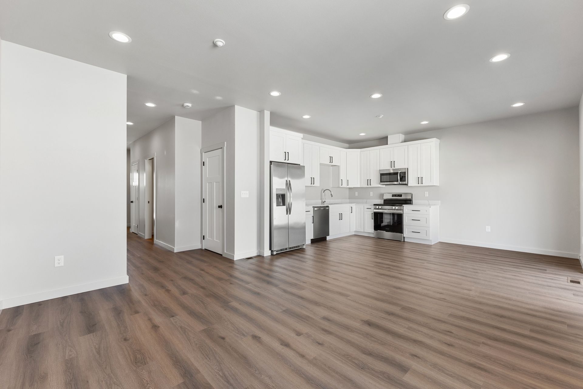 Open-concept living space with kitchen, featuring white cabinets, stainless steel appliances, and dark wood floors.