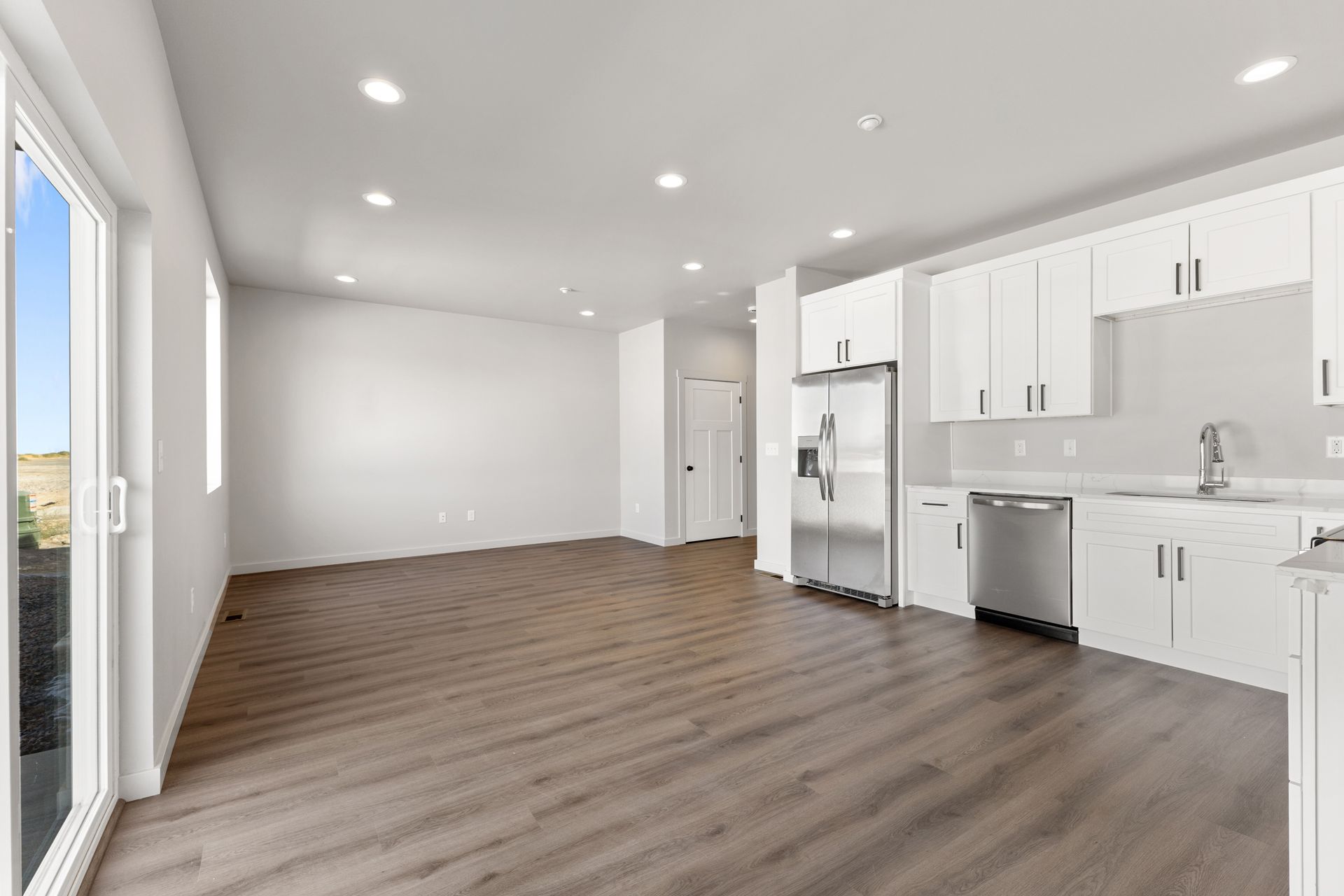 Open-concept kitchen with white cabinets, stainless steel appliances, and hardwood floors; sliding door to outside.