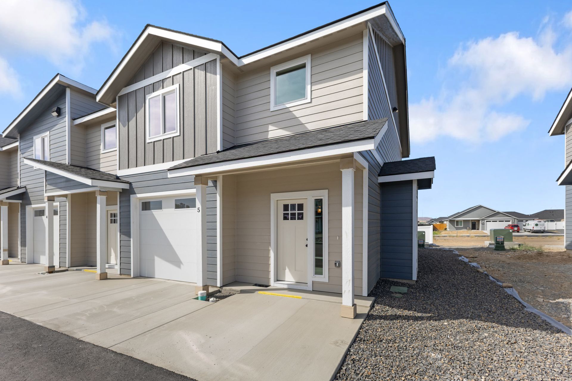 Row of beige and blue townhouses with attached garages under a blue sky.