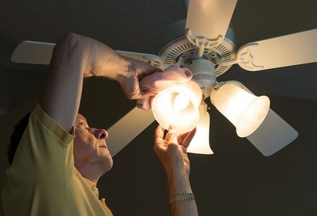 man installing dim yellow light bulb on the ceiling fan