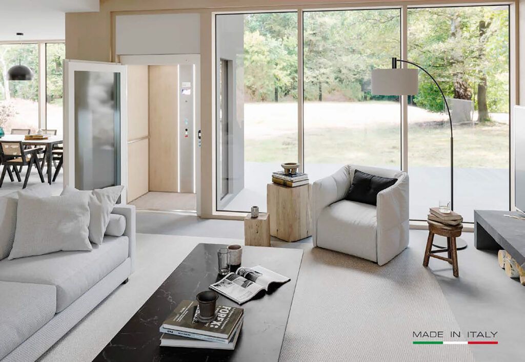 Soggiorno moderno con ampie finestre, divano bianco, poltrona e tavolino da caffè scuro.