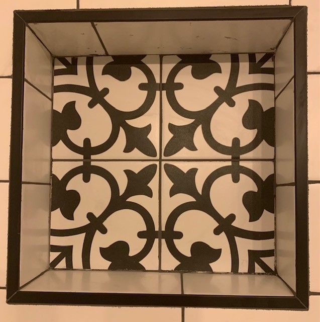 Square inset with decorative tiles: black and white floral pattern surrounded by a dark metal frame.