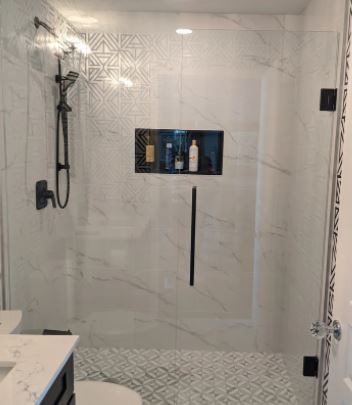 Modern shower with black fixtures, white marble-look tile, and decorative patterned tile in the back.