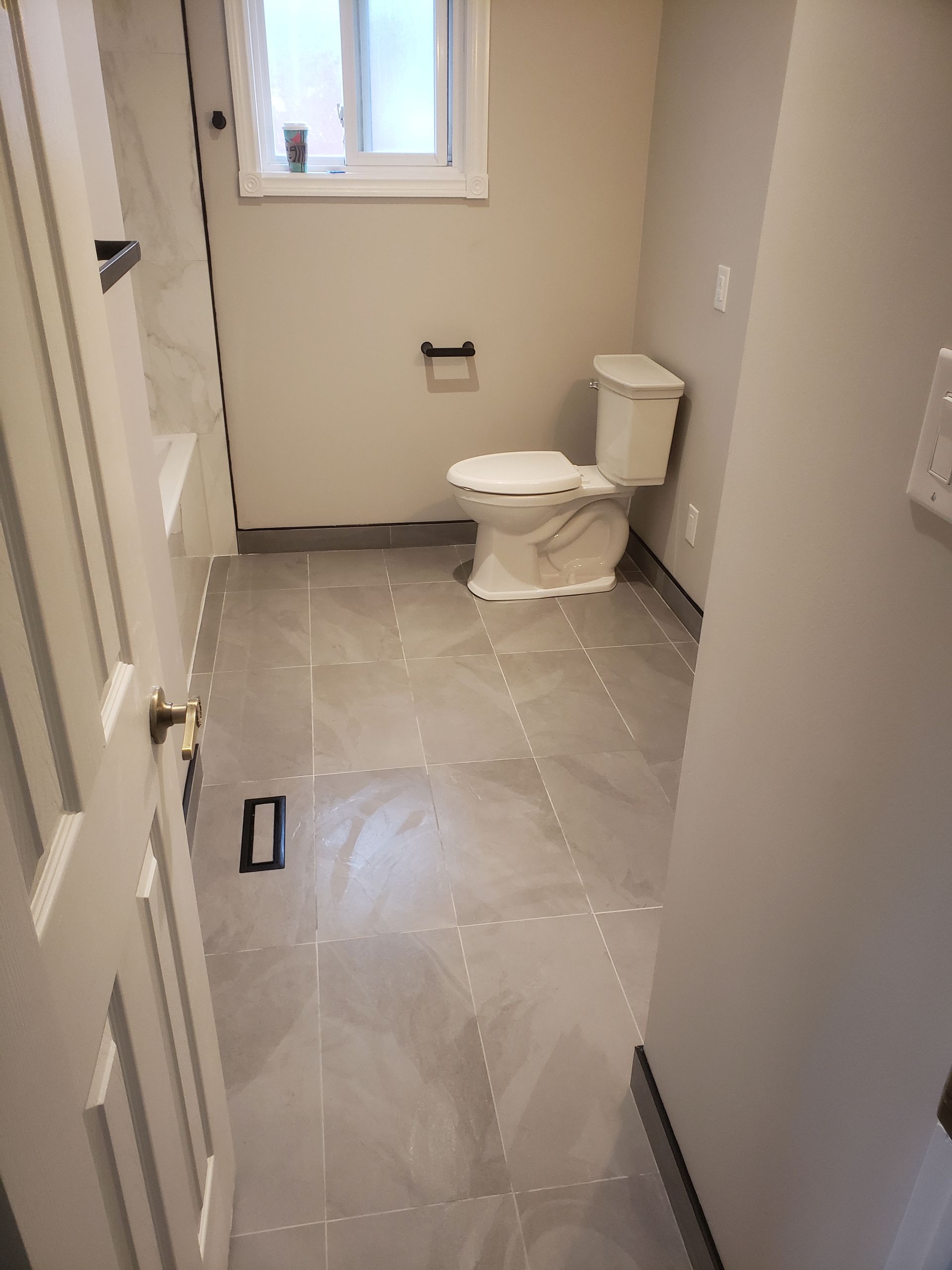 Bathroom with gray tiled floor, white toilet, small window, and gray walls.