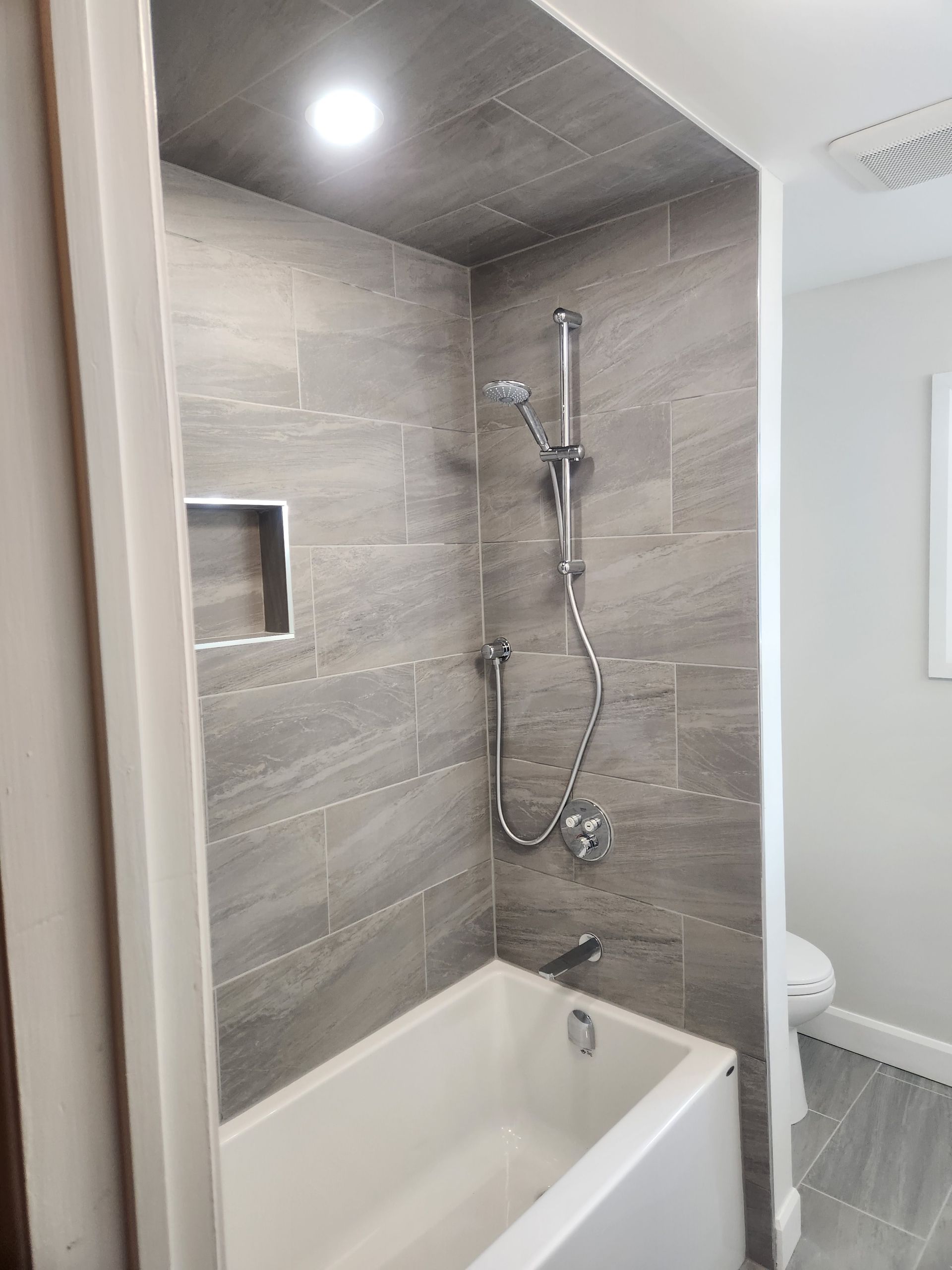 Bathroom with gray tiled shower, bathtub, and grab bar.