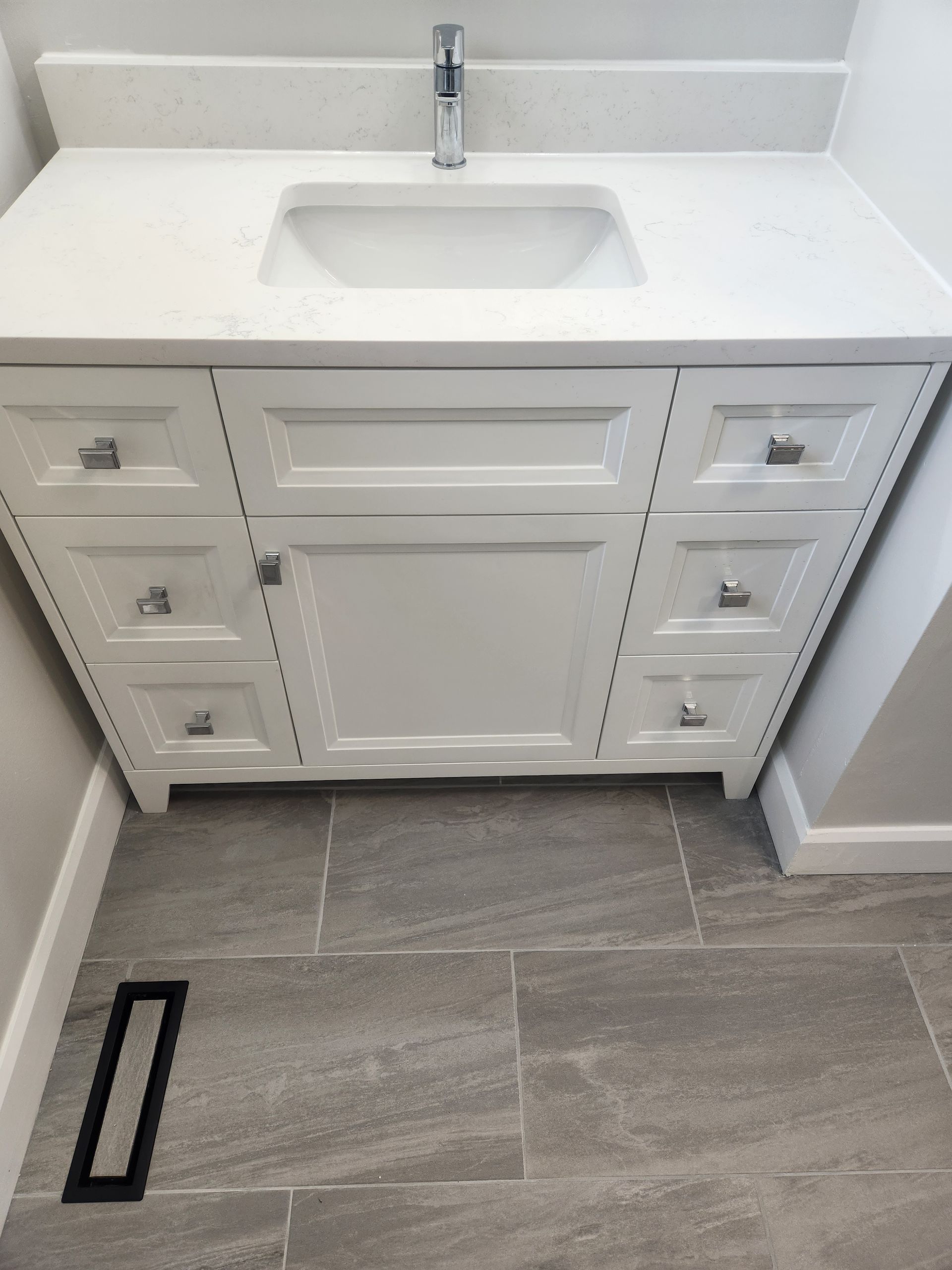 White bathroom vanity with a sink, on gray tiled floor.