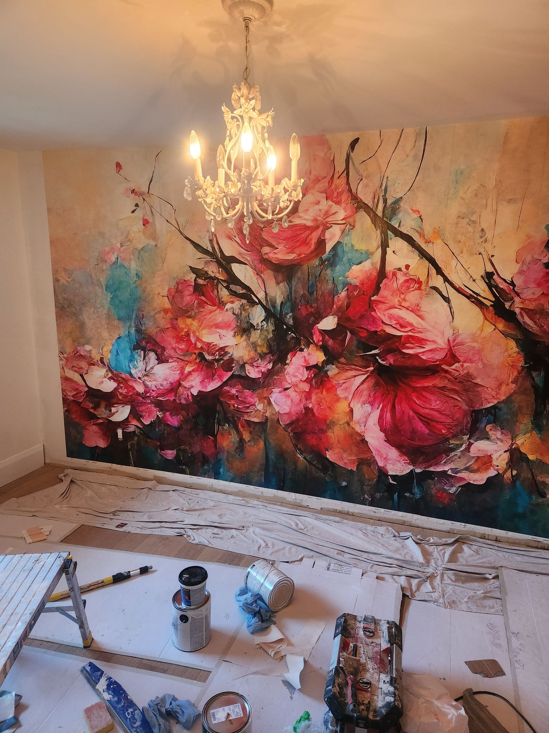 Floral mural with chandelier, painting supplies in front, white walls, and floor.