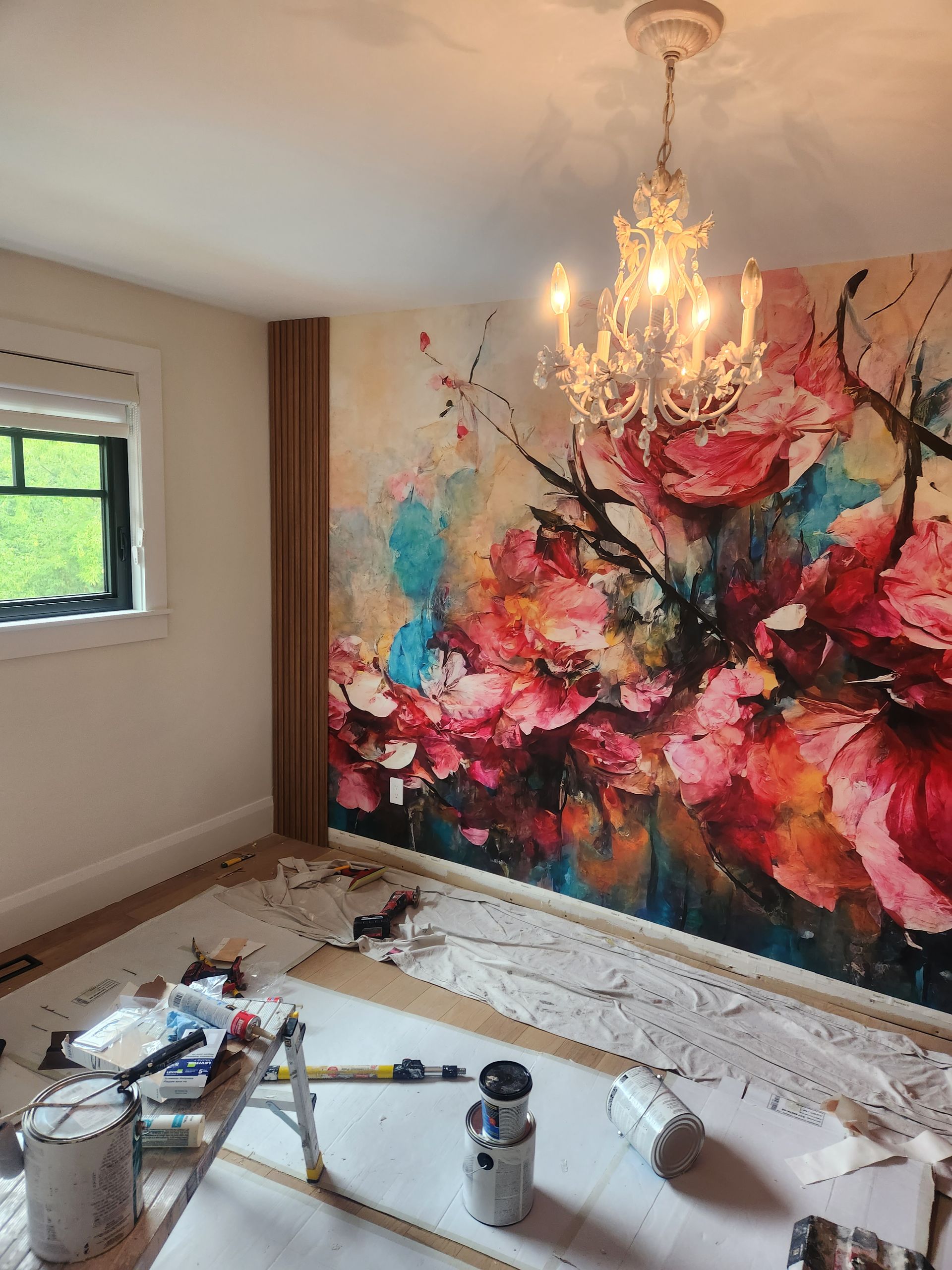 Room with floral mural, chandelier, and paint supplies on the floor.