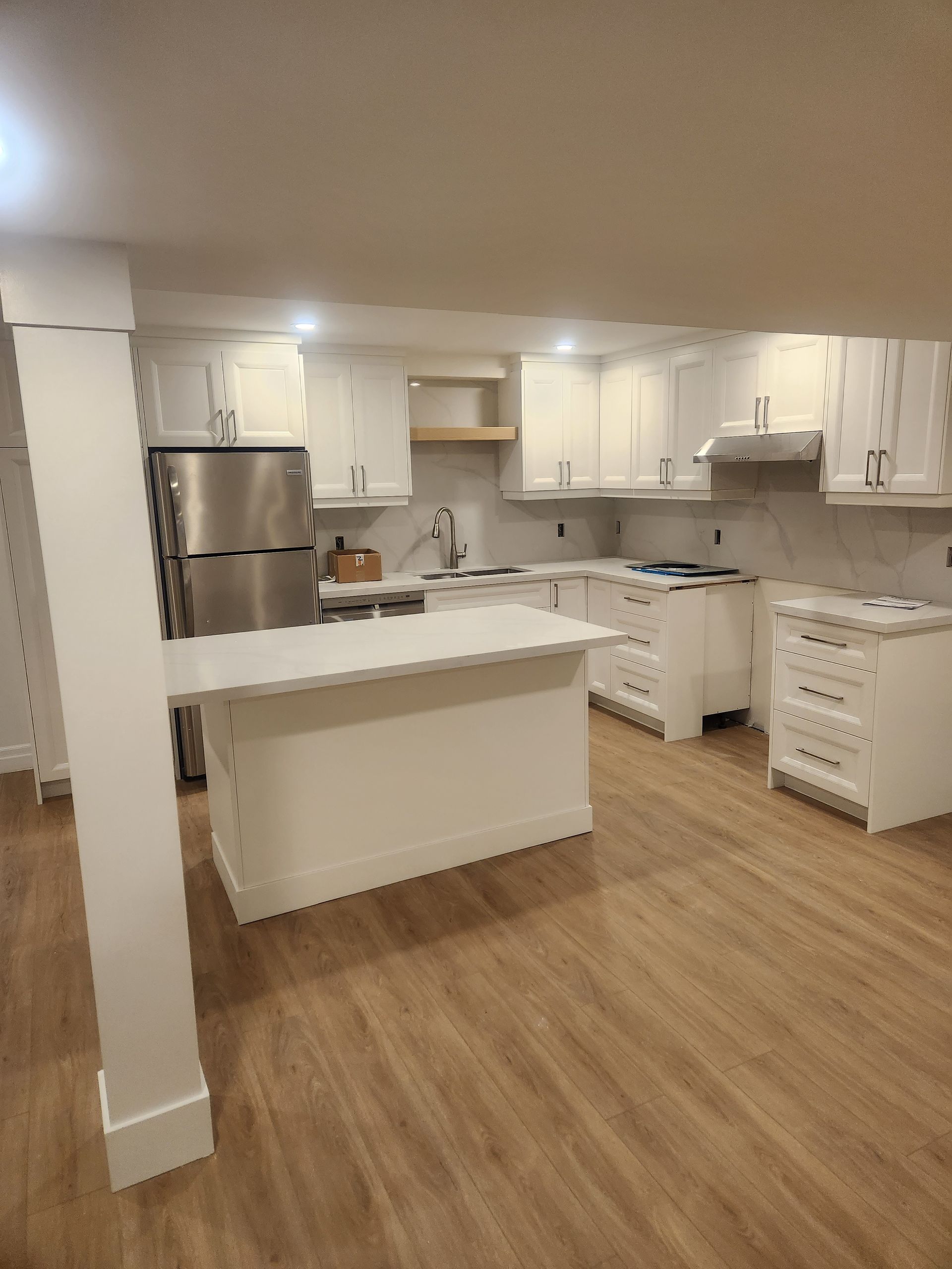 White kitchen with island, stainless steel appliances, and wood-look flooring.
